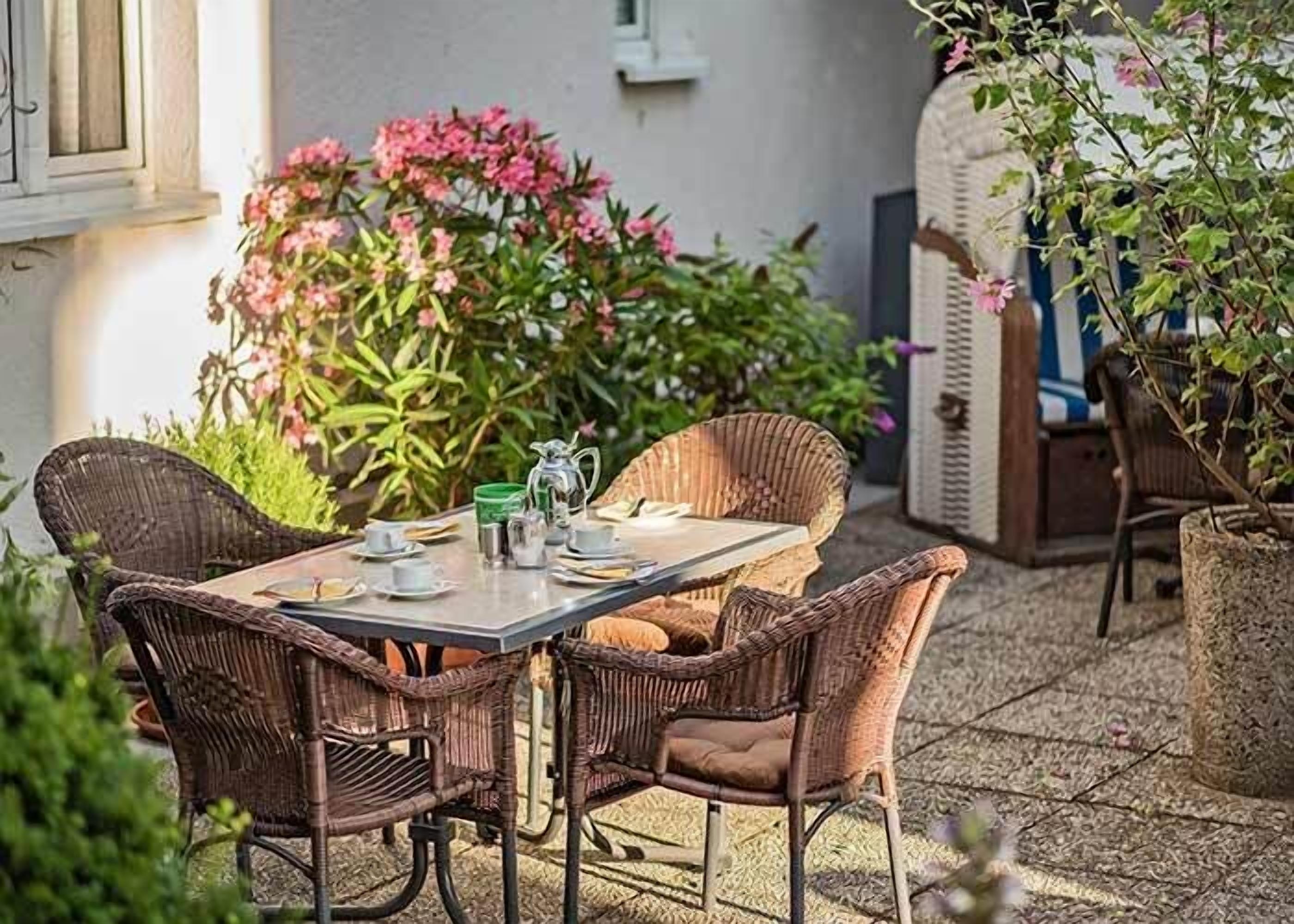 Un patio al aire libre con una mesa lista para cuatro personas, rodeado de sillas de mimbre.