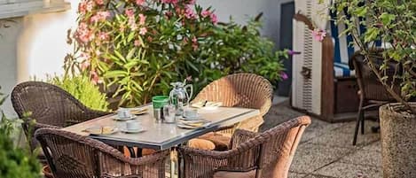 Un patio al aire libre con una mesa lista para cuatro personas, rodeado de sillas de mimbre.