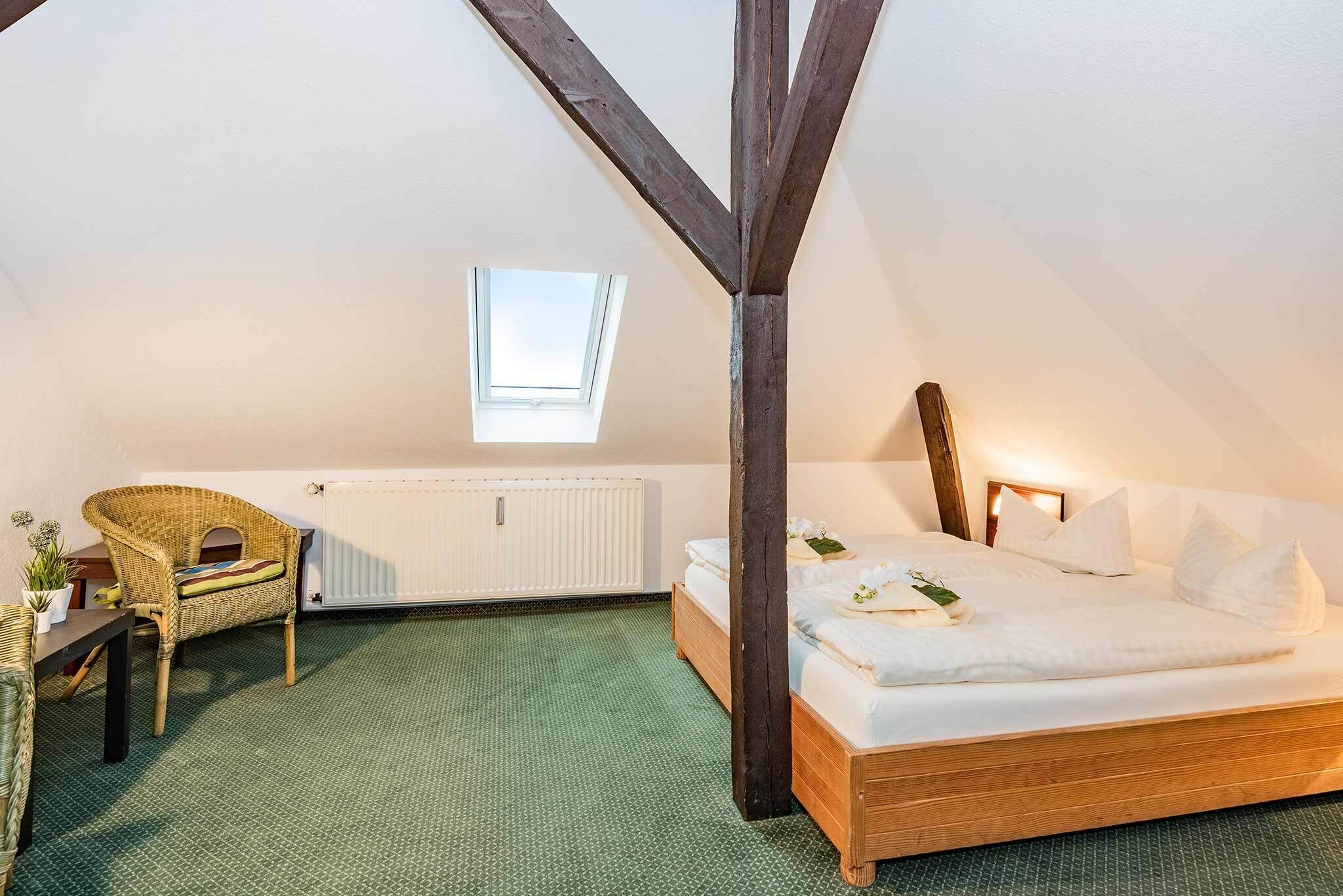 Une chambre avec un plafond en pente, un lit, une chaise, une petite table et une fenêtre.