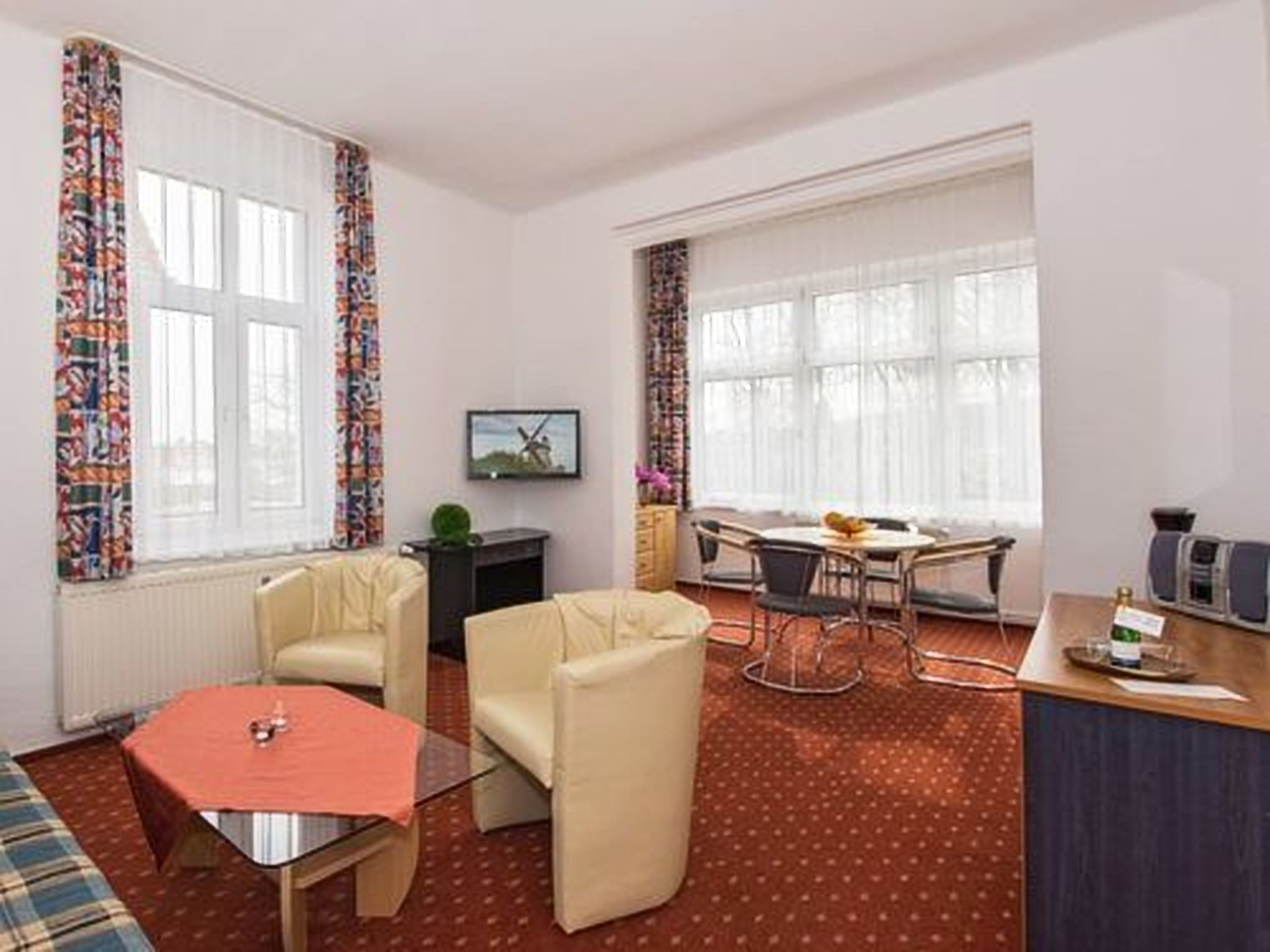 A room with a sofa, a small table, a dining table with chairs, and a kitchen area with a counter and appliances.