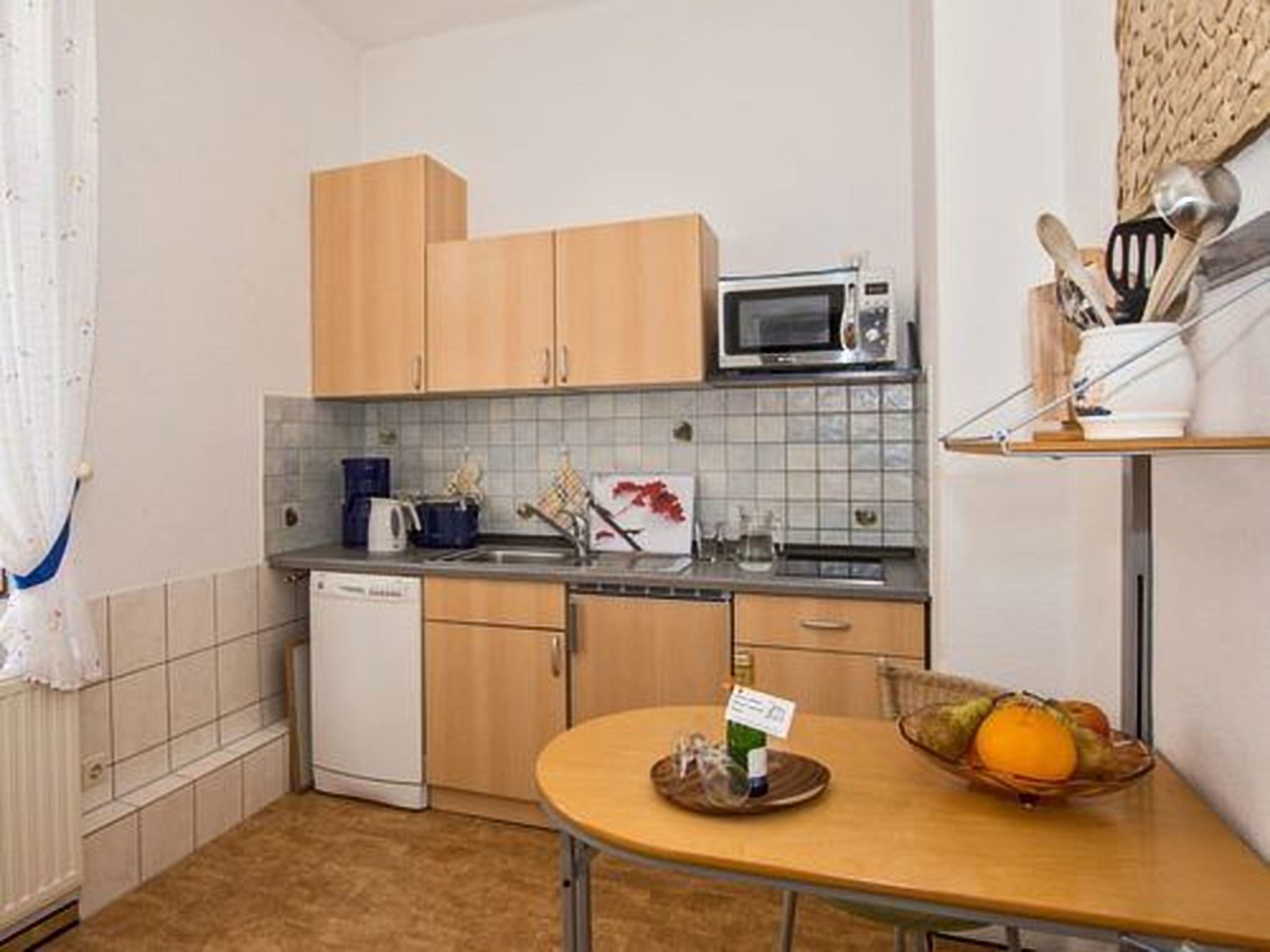 Cocina compacta con armarios de madera, microondas y una pequeña mesa de comedor con frutero.