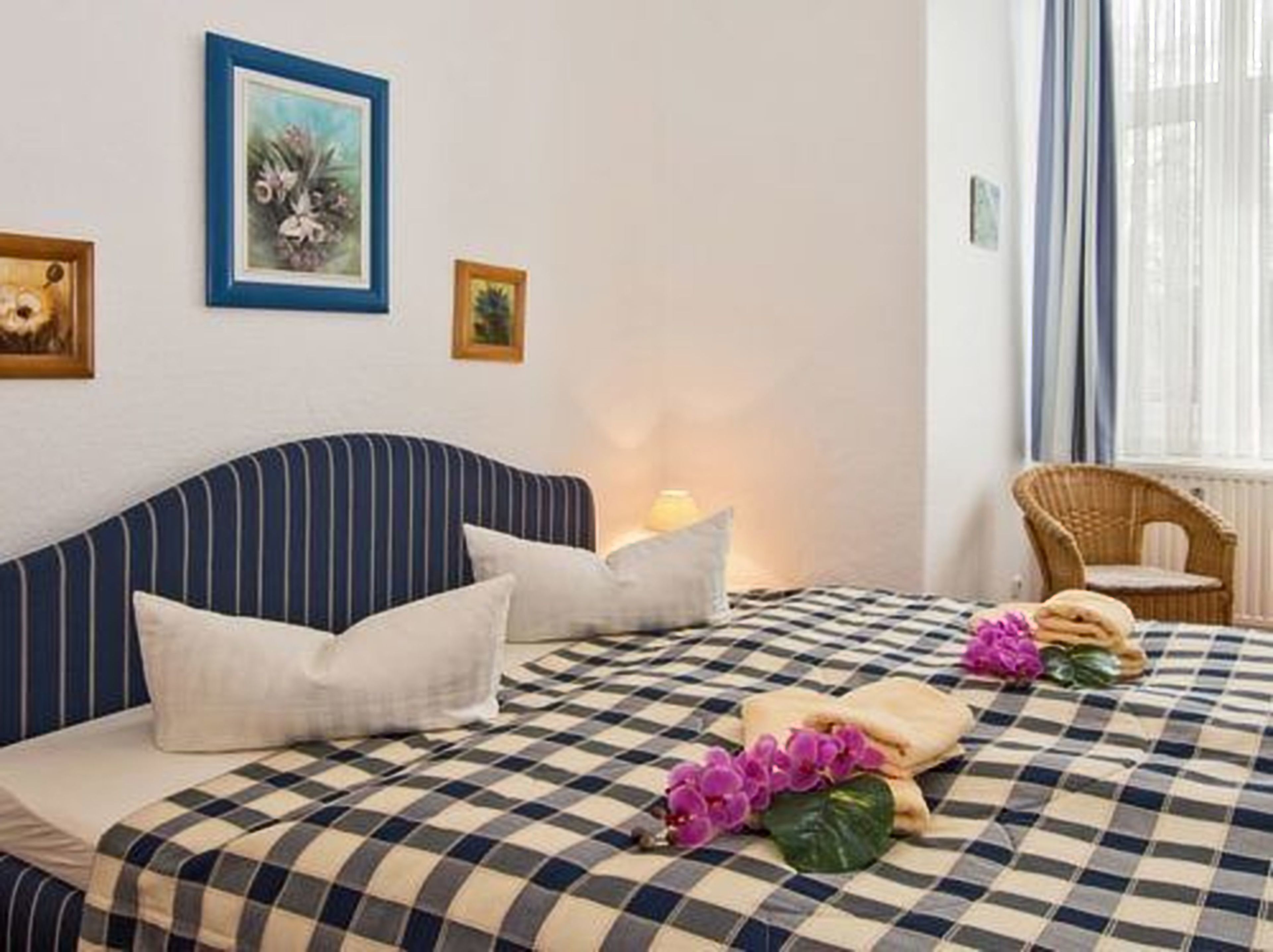 Un dormitorio con cabecera a rayas, colcha de cuadros y una silla de mimbre junto a la ventana.