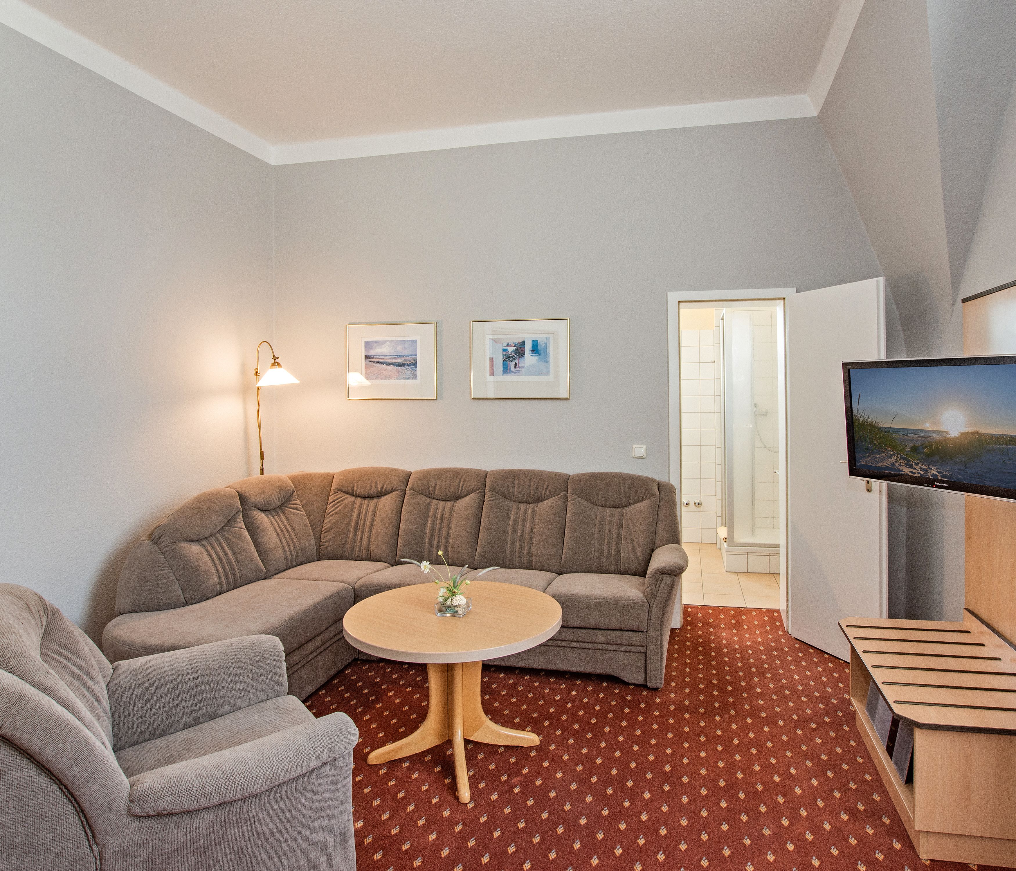 Ein Wohnzimmer mit einer gebogenen Couch, einem runden Couchtisch, einem Fernseher und gerahmten Bildern an der Wand.