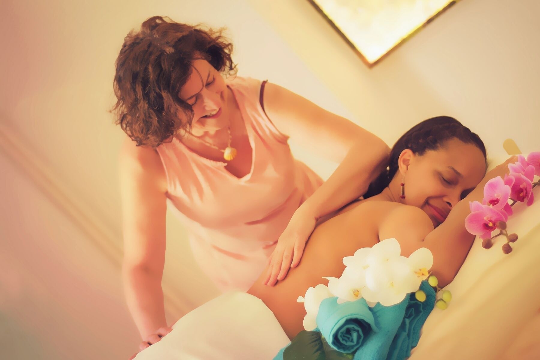 A massage therapy session in a room with a bed, pillows, and flowers.