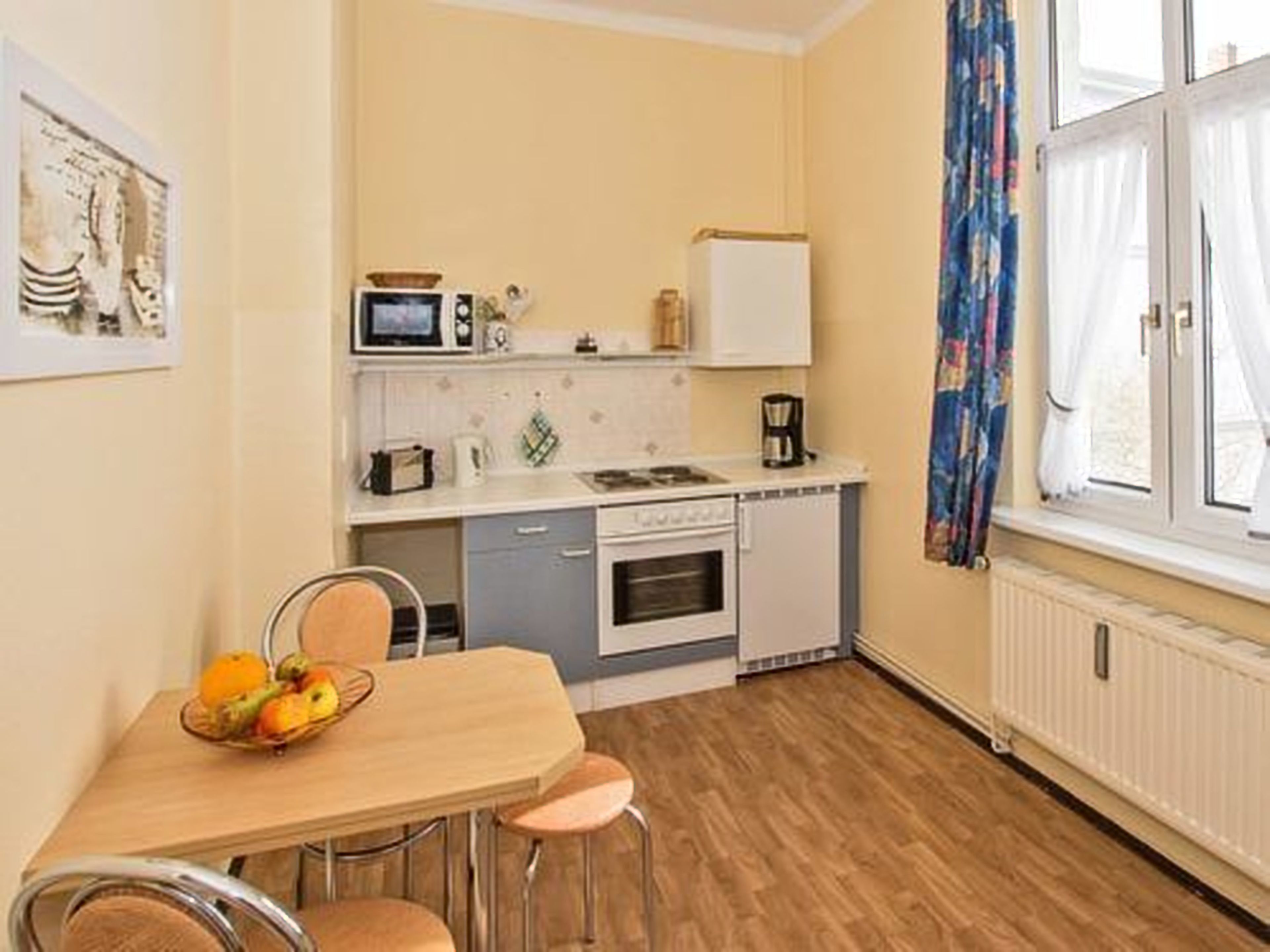 A compact kitchen with a microwave, toaster, and coffee maker on the countertop, a small oven, and a dining table with chairs.