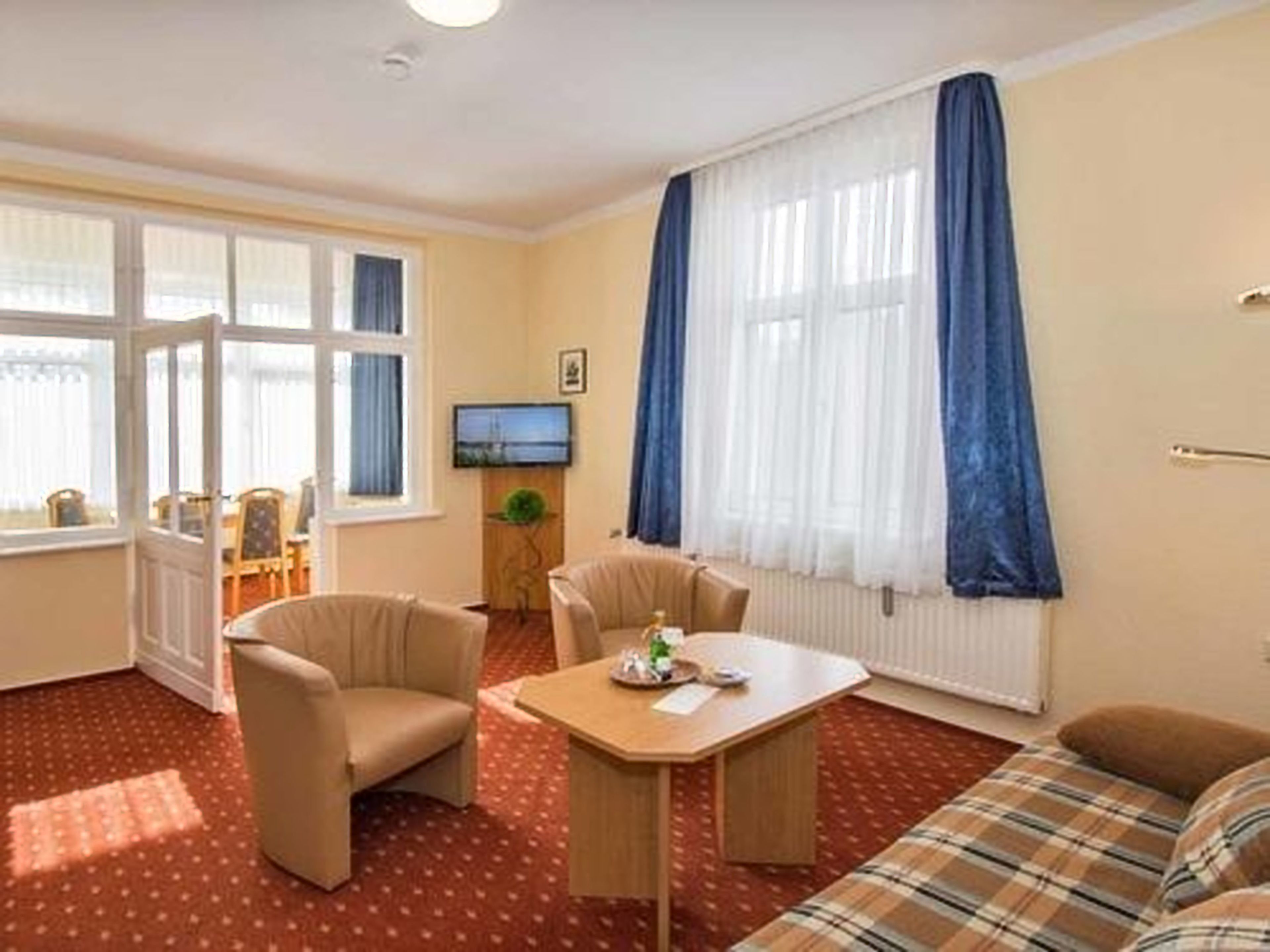 Una habitación con sofá, dos sillones, una mesita y un televisor en la pared.