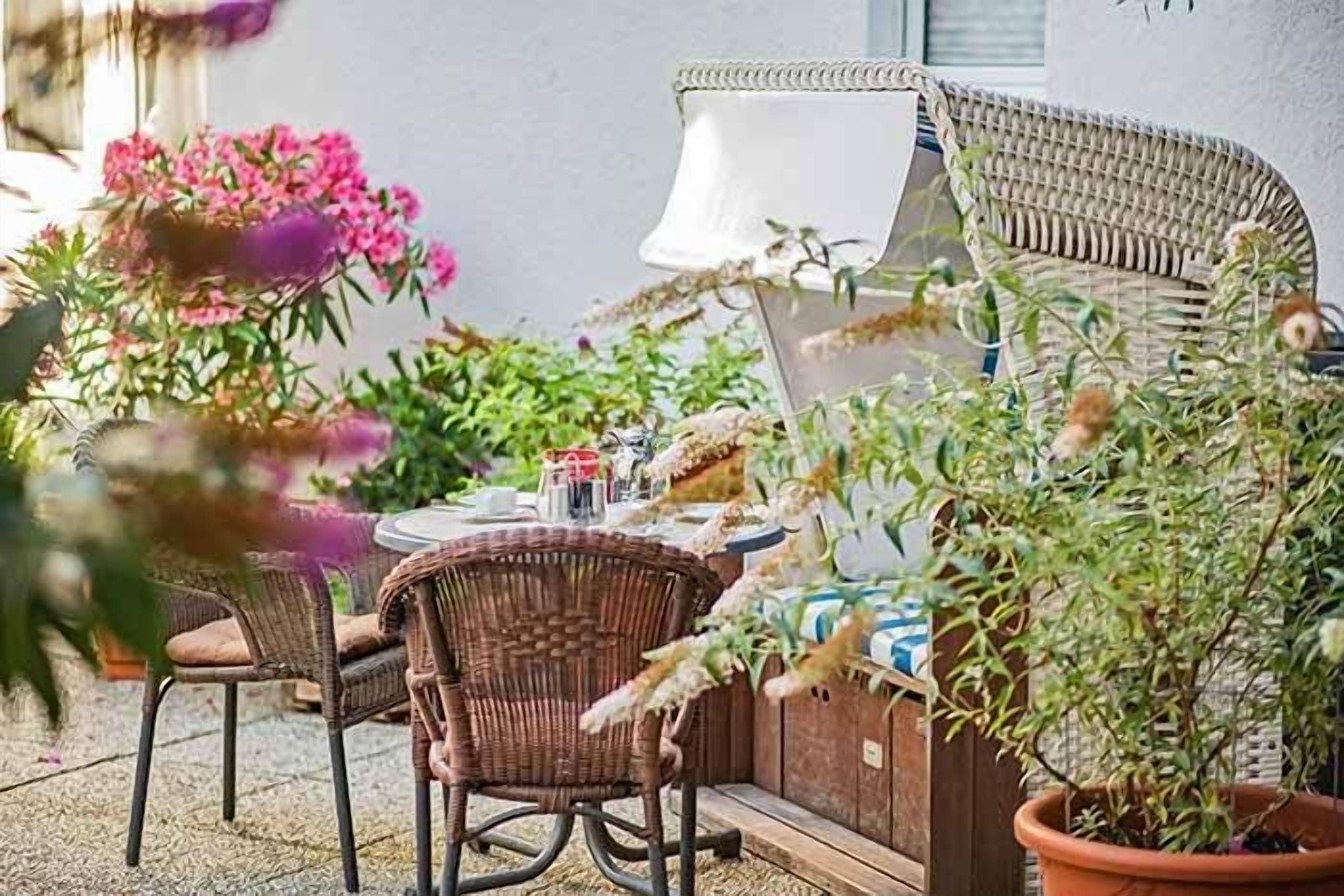 Une terrasse extérieure aménagée avec des meubles en osier, une table dressée pour le repas et des plantes en pot.