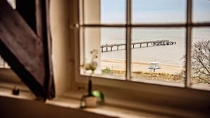 Une vue à travers une fenêtre sur une plage, avec une jetée qui s’avance dans l’eau.