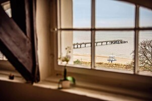 Vista a través de una ventana de una playa con un muelle que se adentra en el agua.