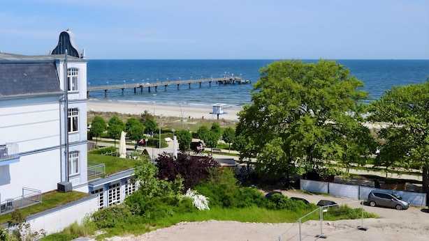 Une vue sur la côte, avec une jetée qui s’avance dans la mer, une plage et un bâtiment doté d’un balcon donnant sur l’eau.