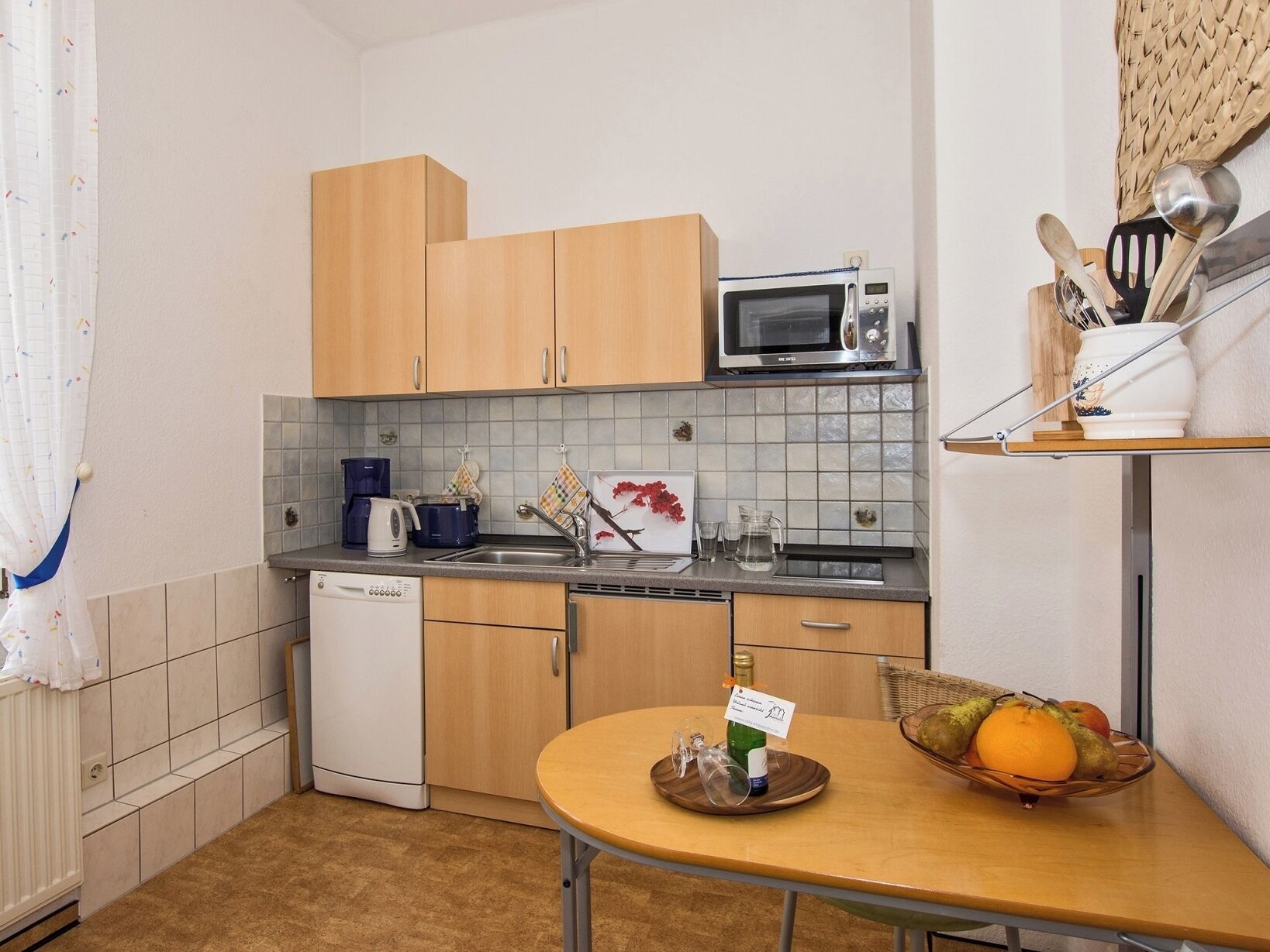 A compact kitchen with wooden cabinets, a microwave, a dishwasher, and a small dining table with a fruit bowl.