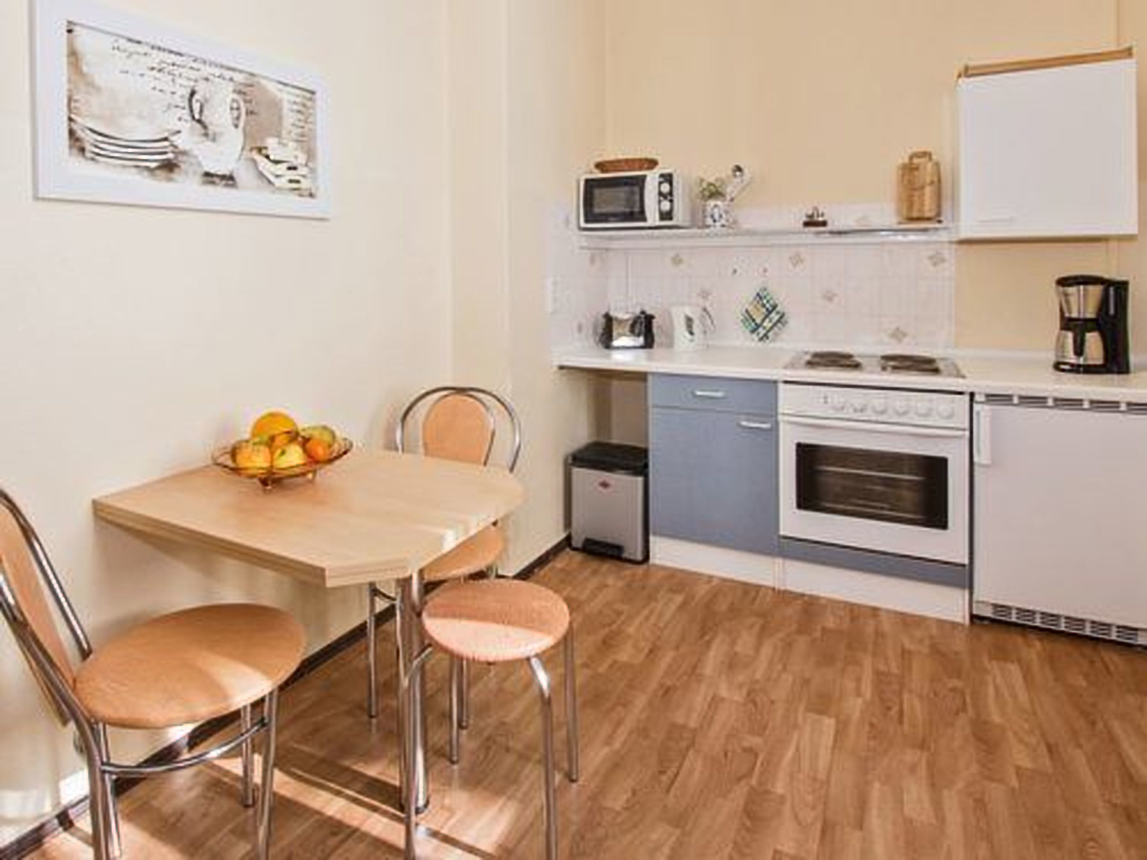 A compact kitchen with a dining area, featuring a microwave, toaster, and coffee maker on the countertop, and a small oven.