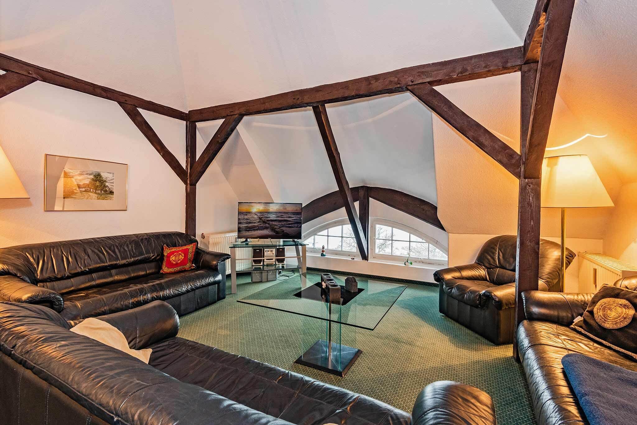 Un loft spacieux avec de hauts plafonds, des poutres apparentes, des canapés en cuir, une table basse en verre et une vue sur l’extérieur.