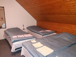 A room with two beds, each with a grey patterned bedspread and white pillows. There is a small bedside table with a lamp and a mirror on the wall. - B & B Hygge (Tranekaer)