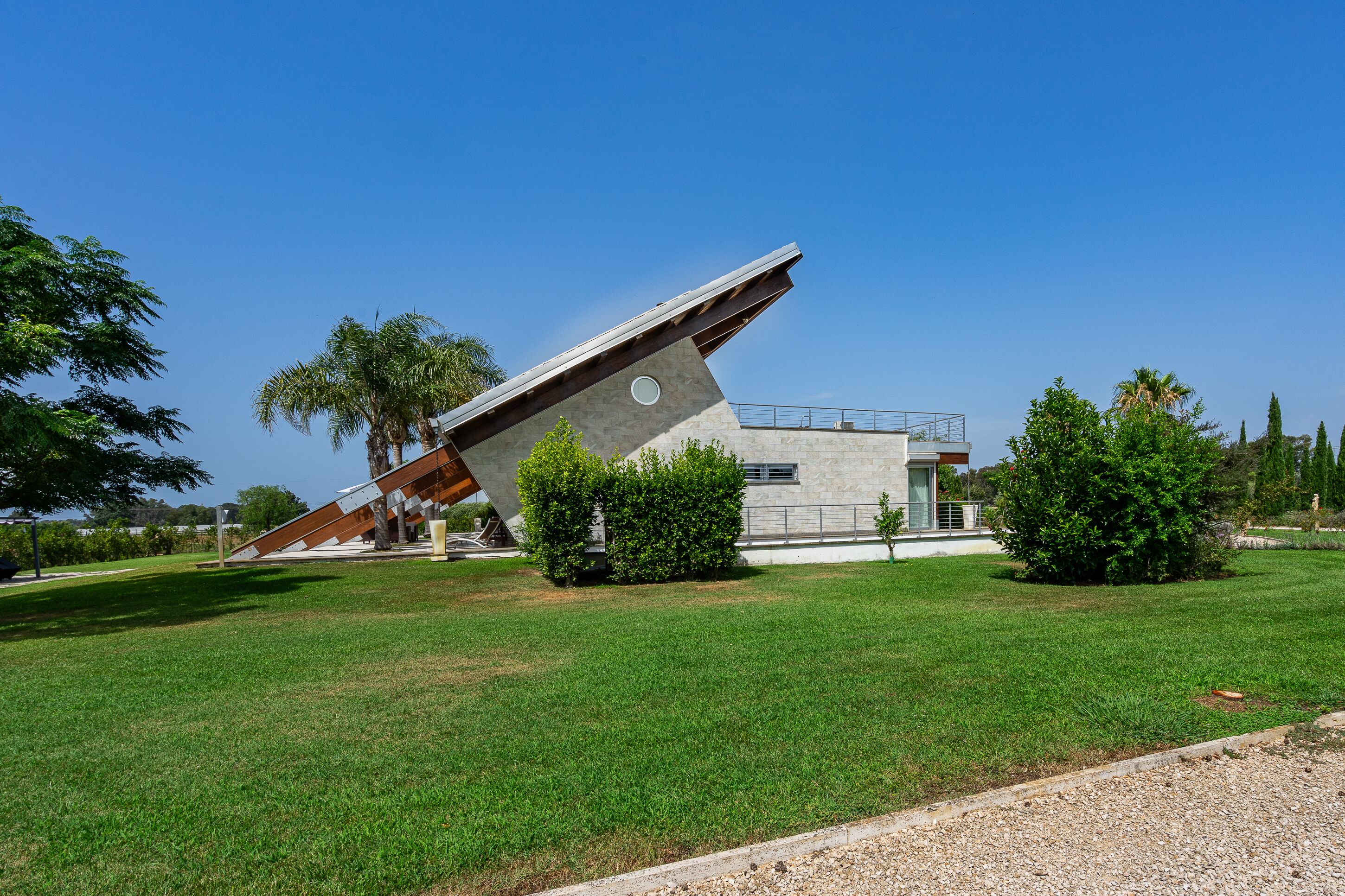 A modern building with a unique slanted roof, surrounded by well-maintained grass and small bushes.
