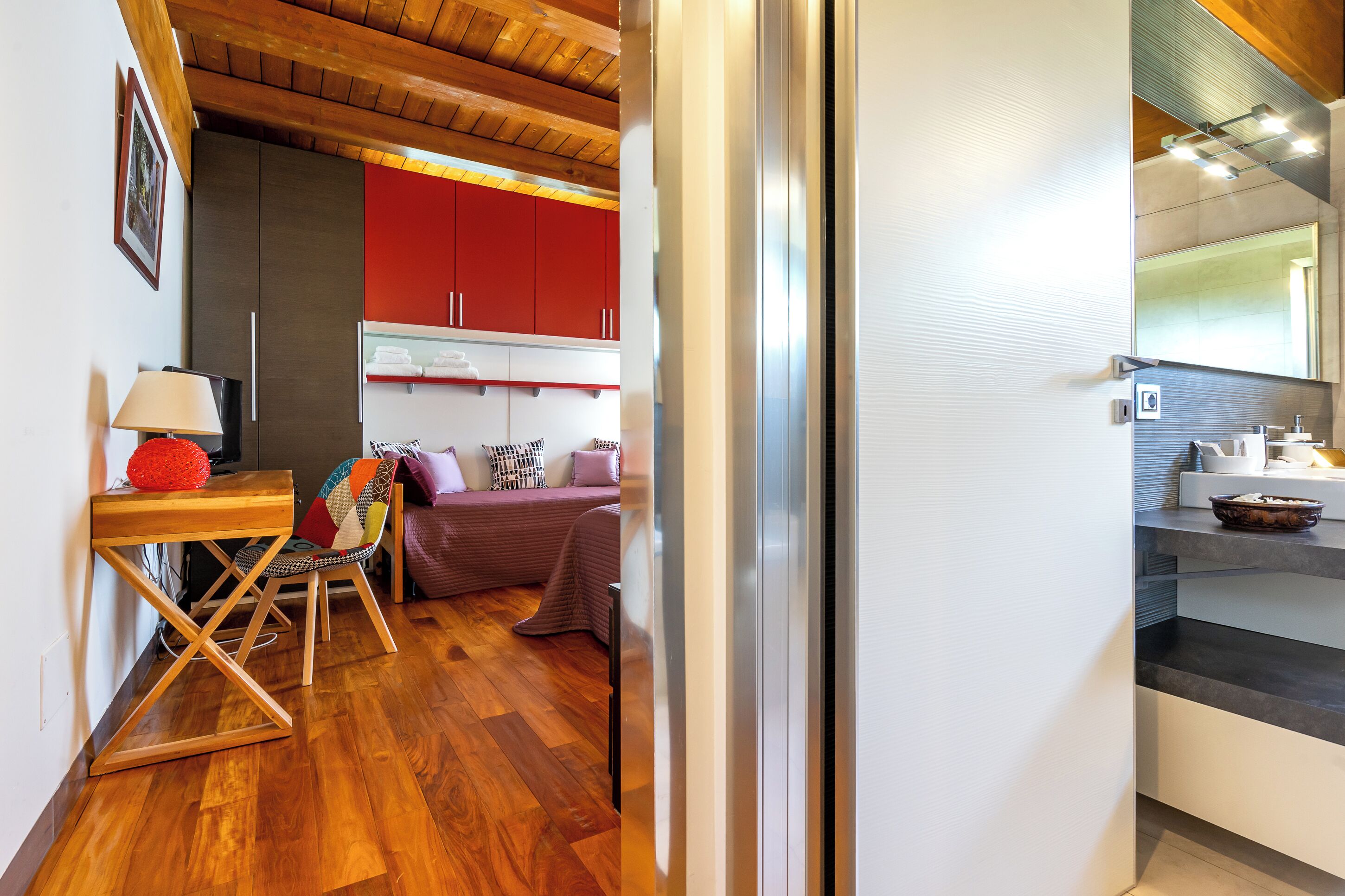 A compact living space with a wooden floor, a dining area with a table and chairs, a sofa, and a kitchenette with a refrigerator and a mirror.