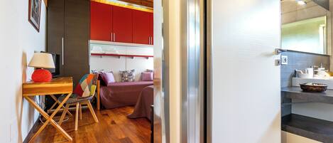 Un espacio habitable compacto con suelo de madera, una zona de comedor con mesa y sillas, un sofá y una kitchenette con refrigerador y espejo.