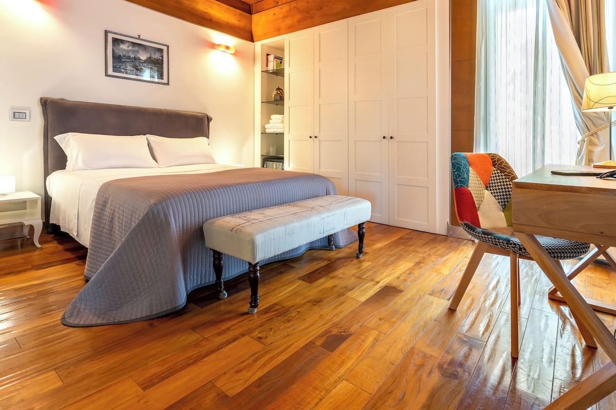 A bedroom with a bed, a bench, a desk, and a wardrobe.