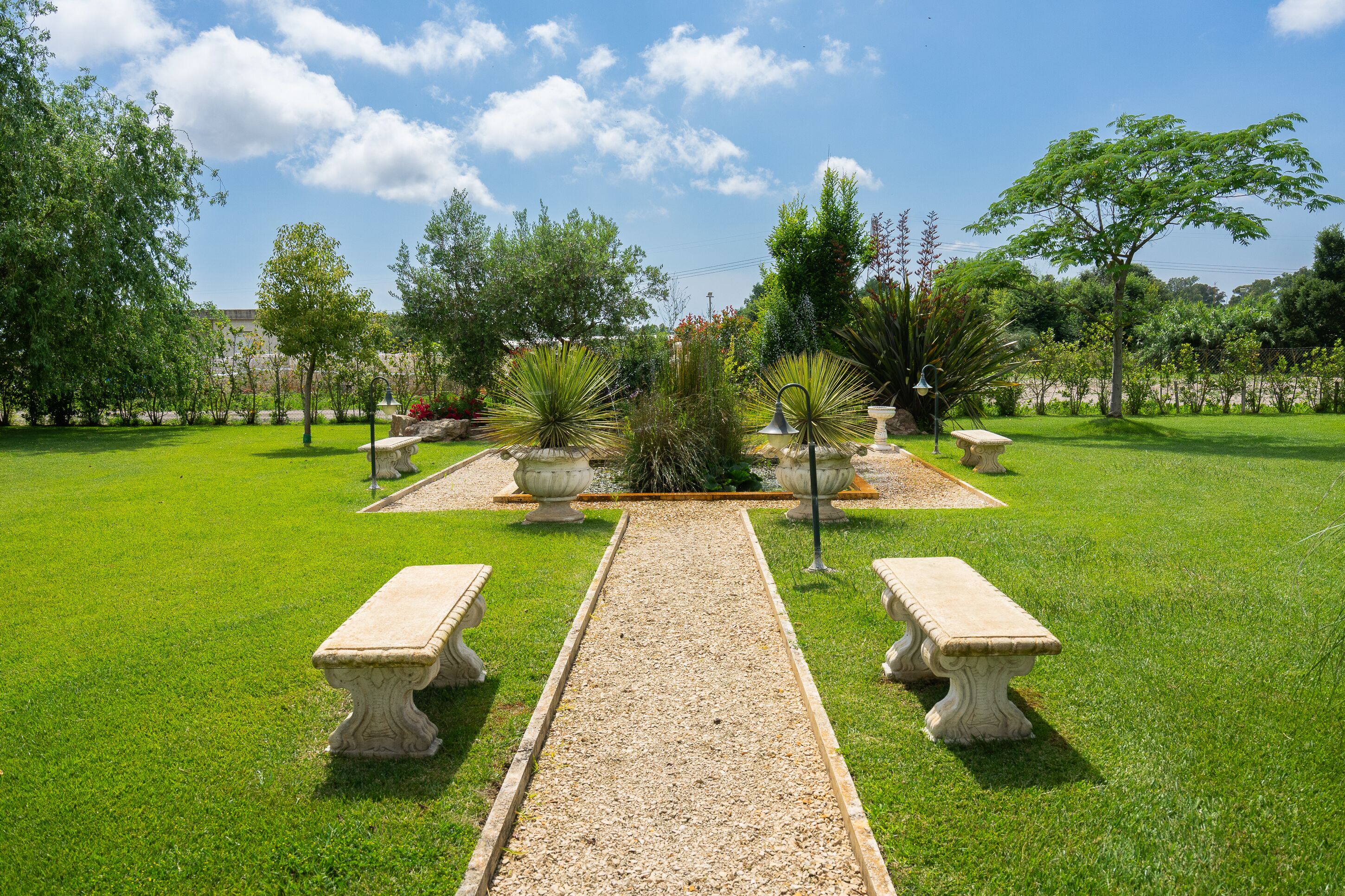 Een tuin met een grindpad, stenen bankjes en verschillende planten.