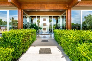 A modern building entrance with a glass facade, a concrete pathway, and green hedges on either side. - Casale delle Ronde B&B (Latina)