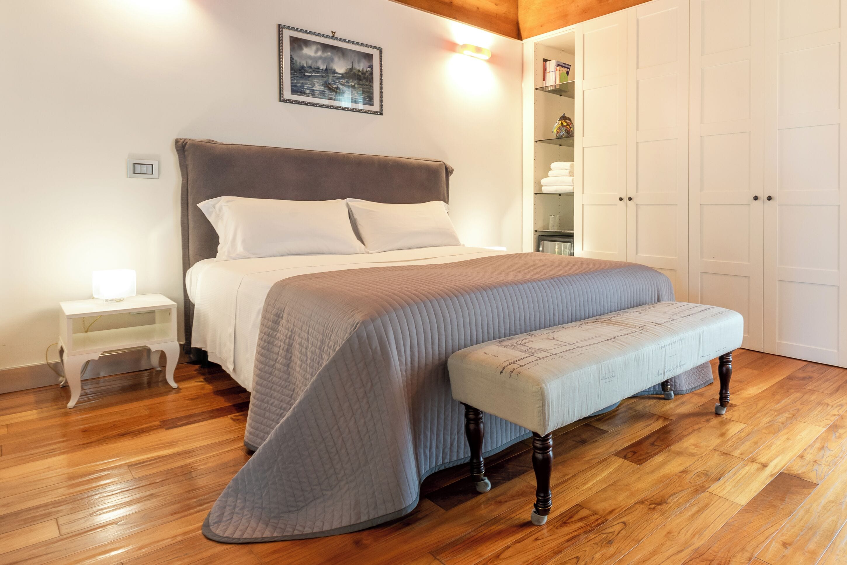 A bedroom with a bed, bedside table, bench, and a wardrobe.