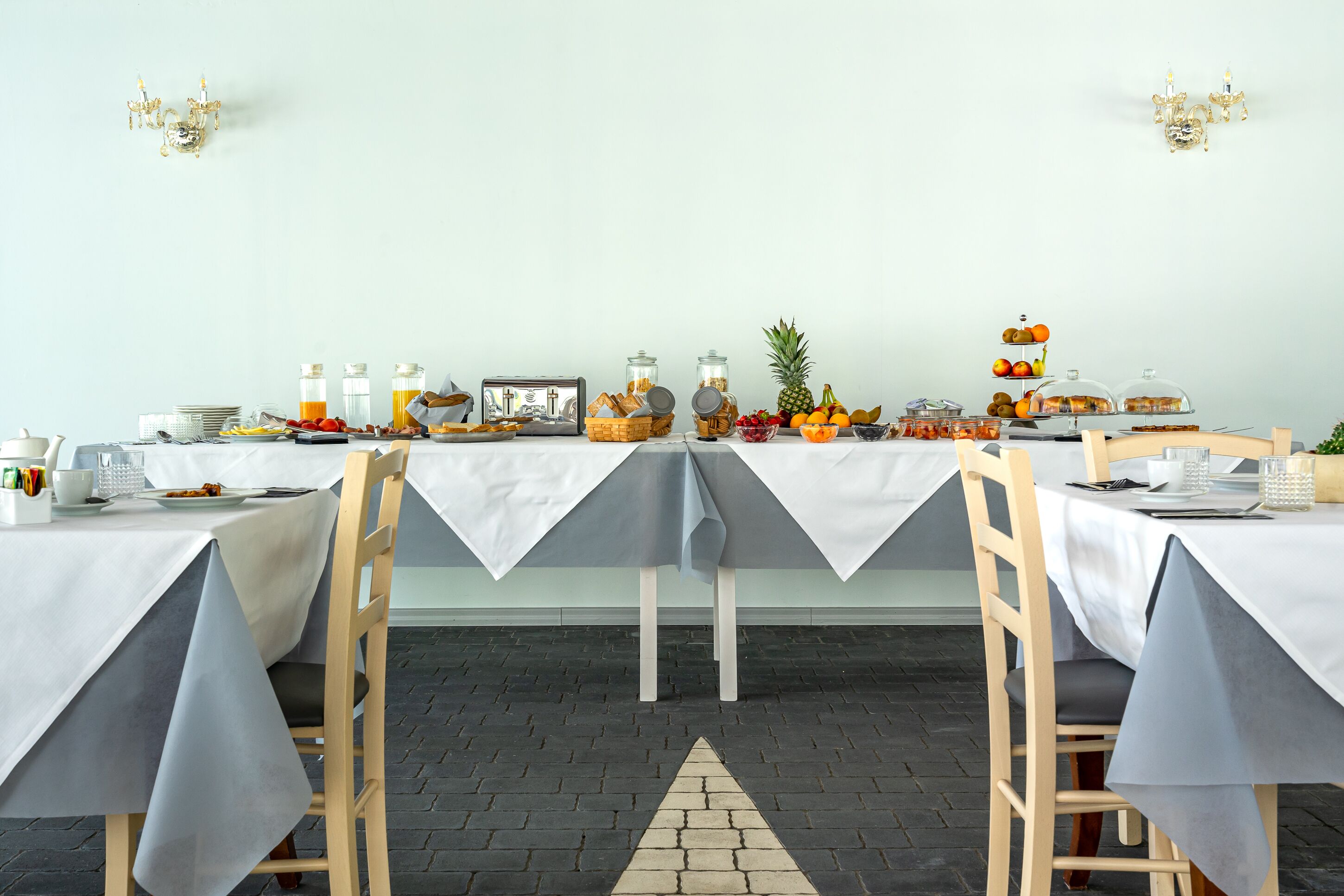 A breakfast buffet setup with tables covered in white tablecloths, various food items, and fruit displayed on the tables.