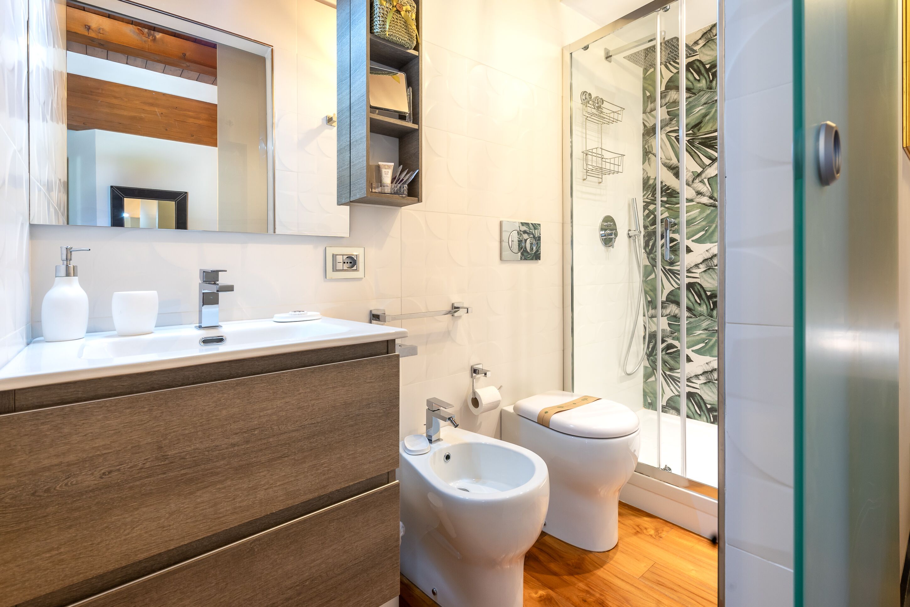 A modern bathroom with a wooden vanity, a bidet, and a shower with a leaf-patterned glass door.