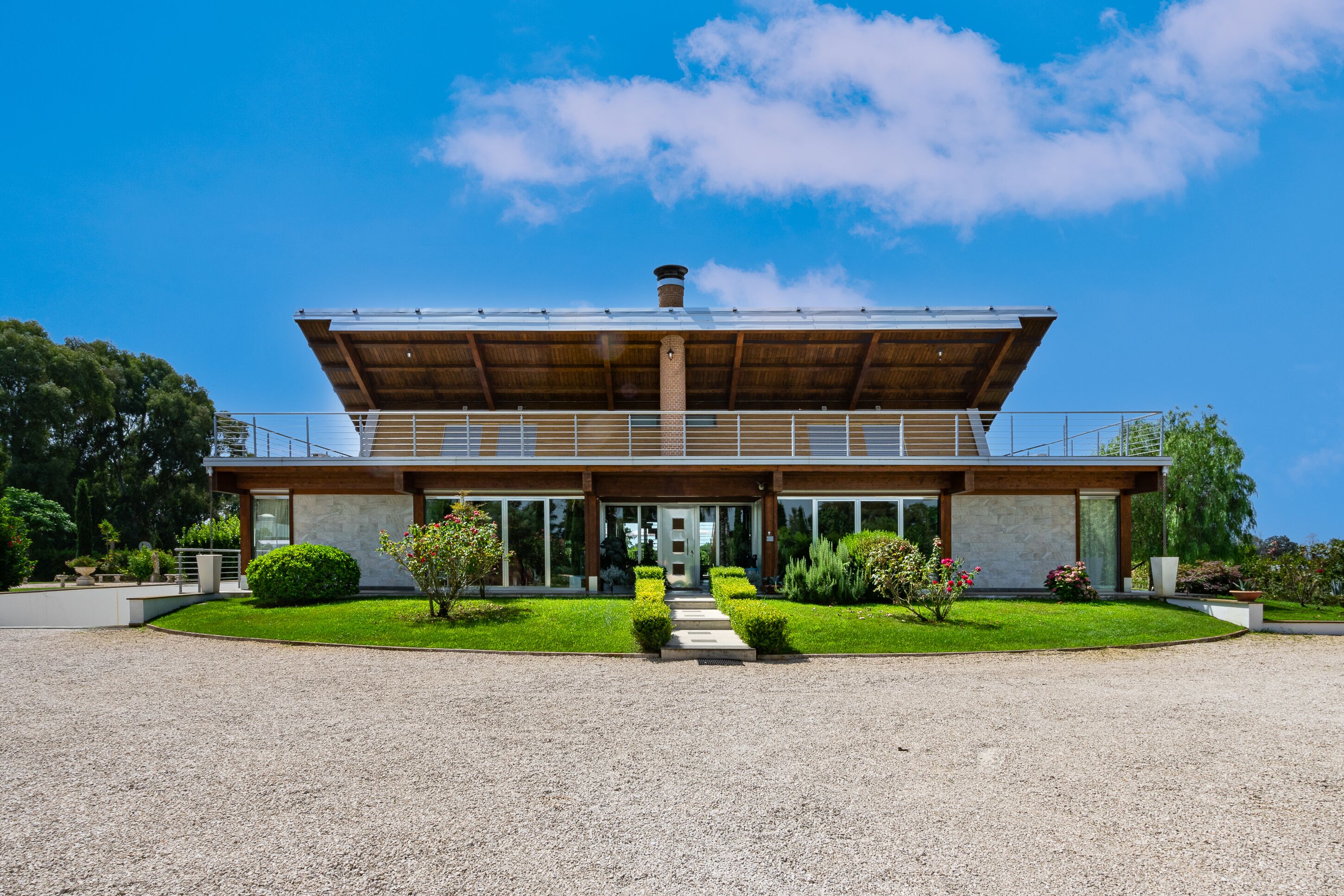 A modern building with a flat roof, large windows, and a gravel driveway.