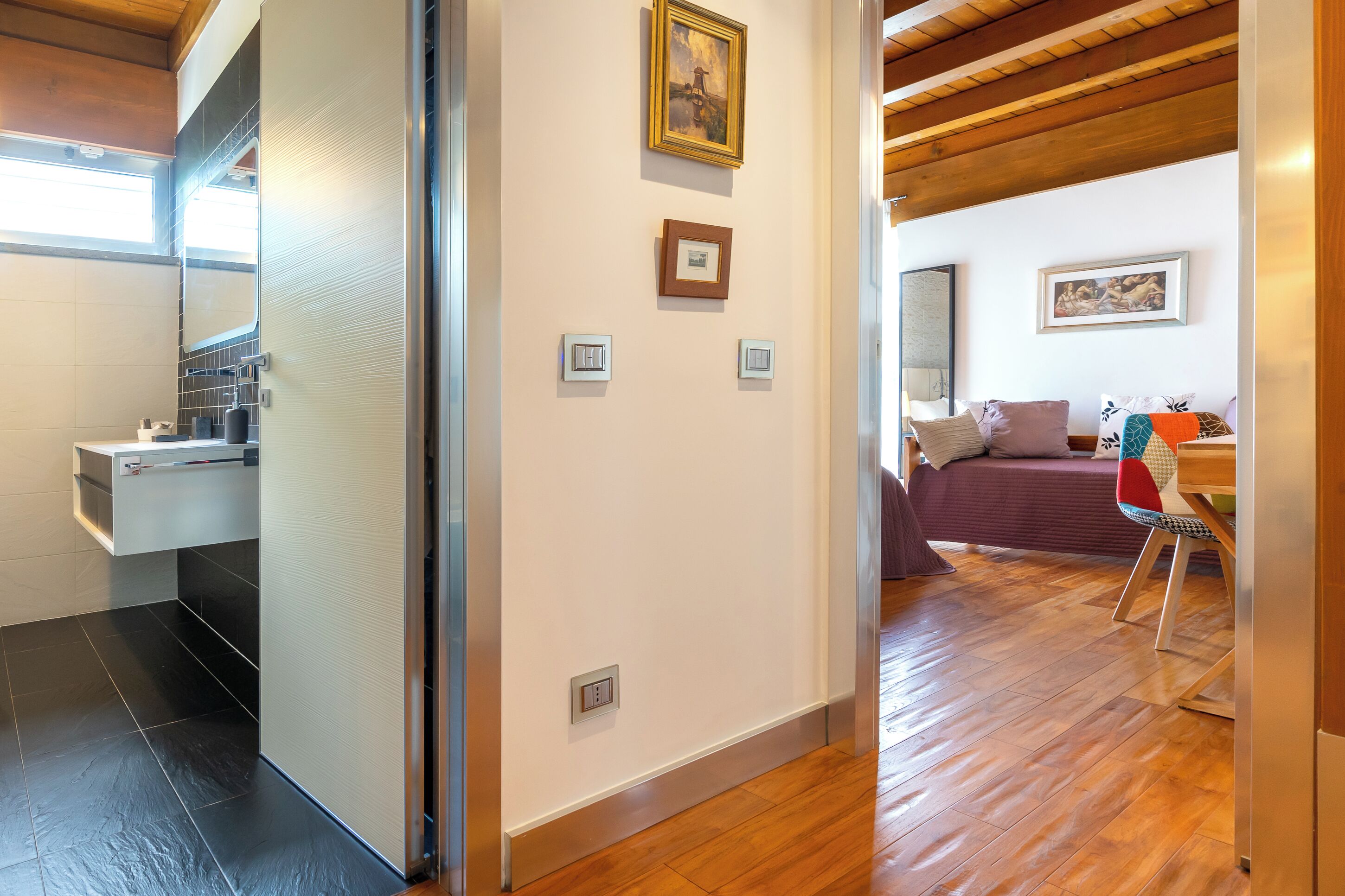 A modern interior with a wooden ceiling, a kitchen area with a built-in oven, a dining area with a table and chairs, and a living area with a sofa and cushions.