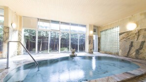 Una amplia piscina interior con borde de mármol, ventanas grandes y una fuente de piedra.