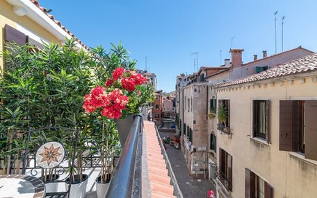 A narrow street with buildings on either side, a tiled roof, and a potted plant with red flowers.