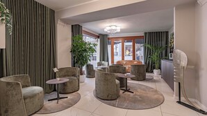 A modern hotel lobby with a seating area featuring round tables and cushioned chairs, a chandelier, and potted plants. - Hotel Grifoni (Venice)