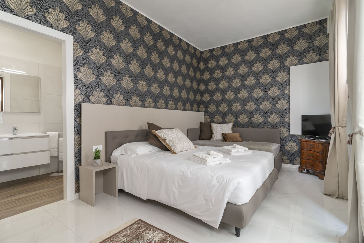 A modern bedroom with a large bed, a bedside table, a dresser, and a television.