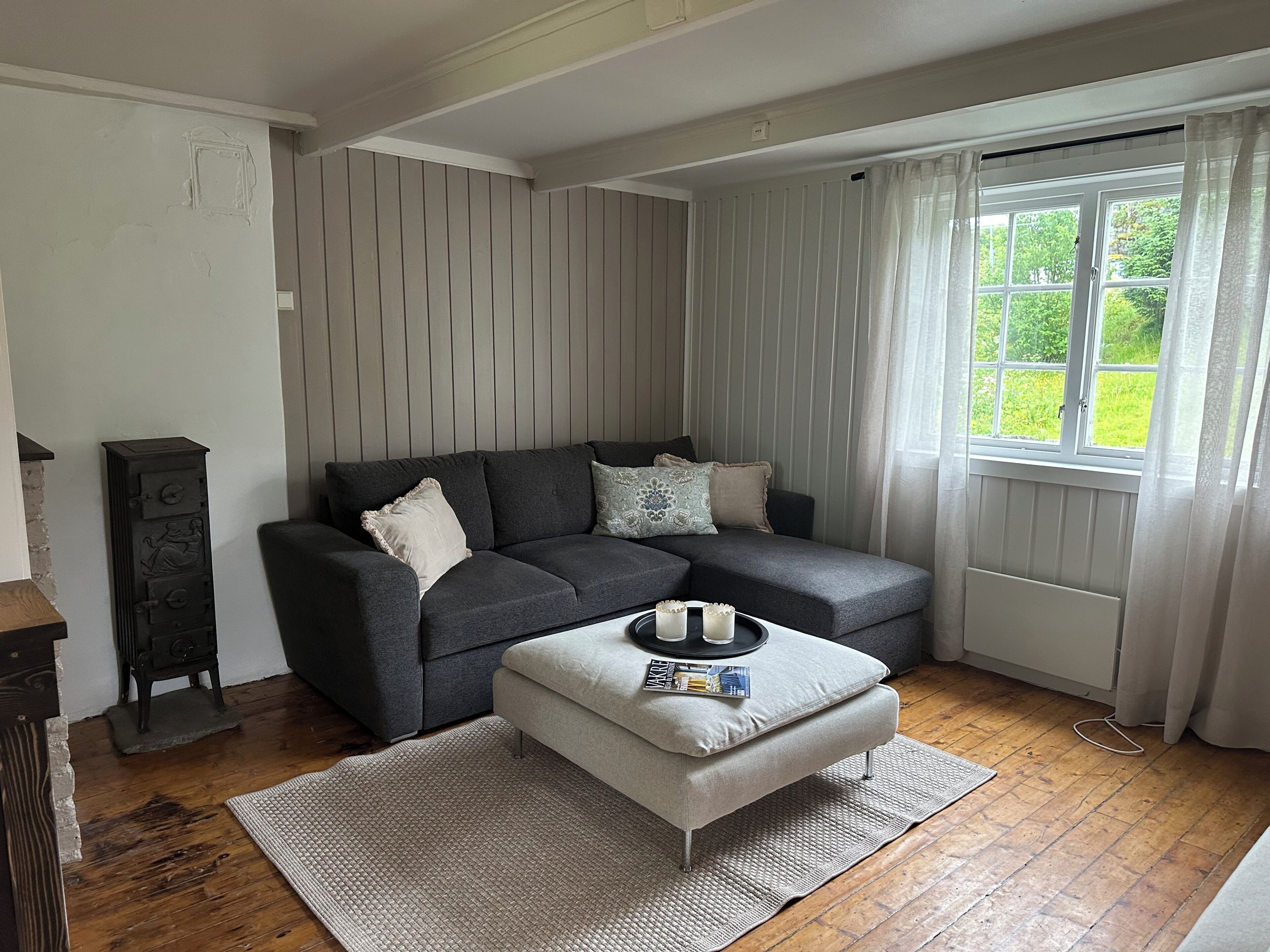 A living room with a grey sofa, a small ottoman, a magazine, and a tray with cups and saucers.