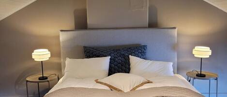 A bedroom with a sloped ceiling, a bed with a patterned quilt, two bedside lamps, and a dark headboard.