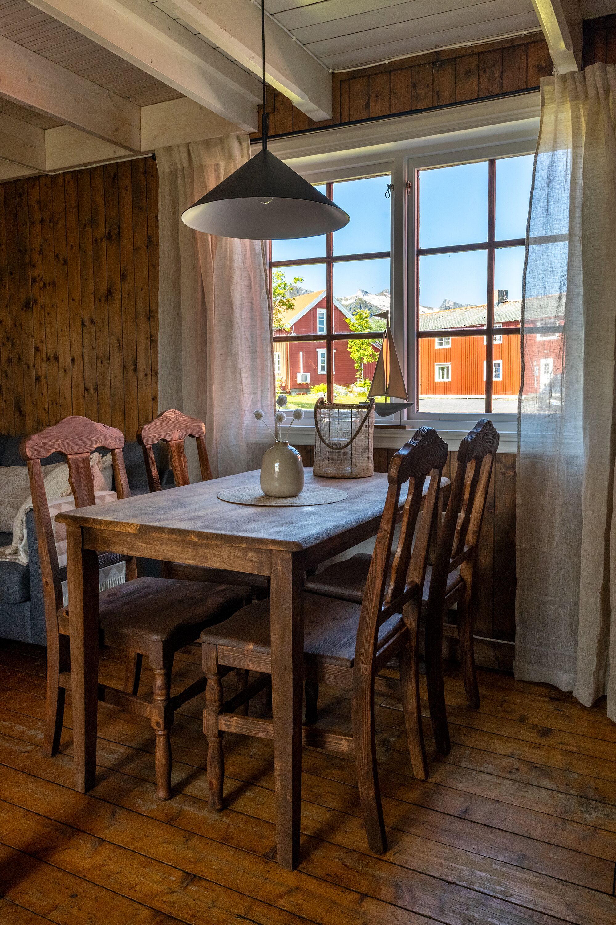 A wooden dining table with chairs, a hanging light fixture, and a window with curtains.