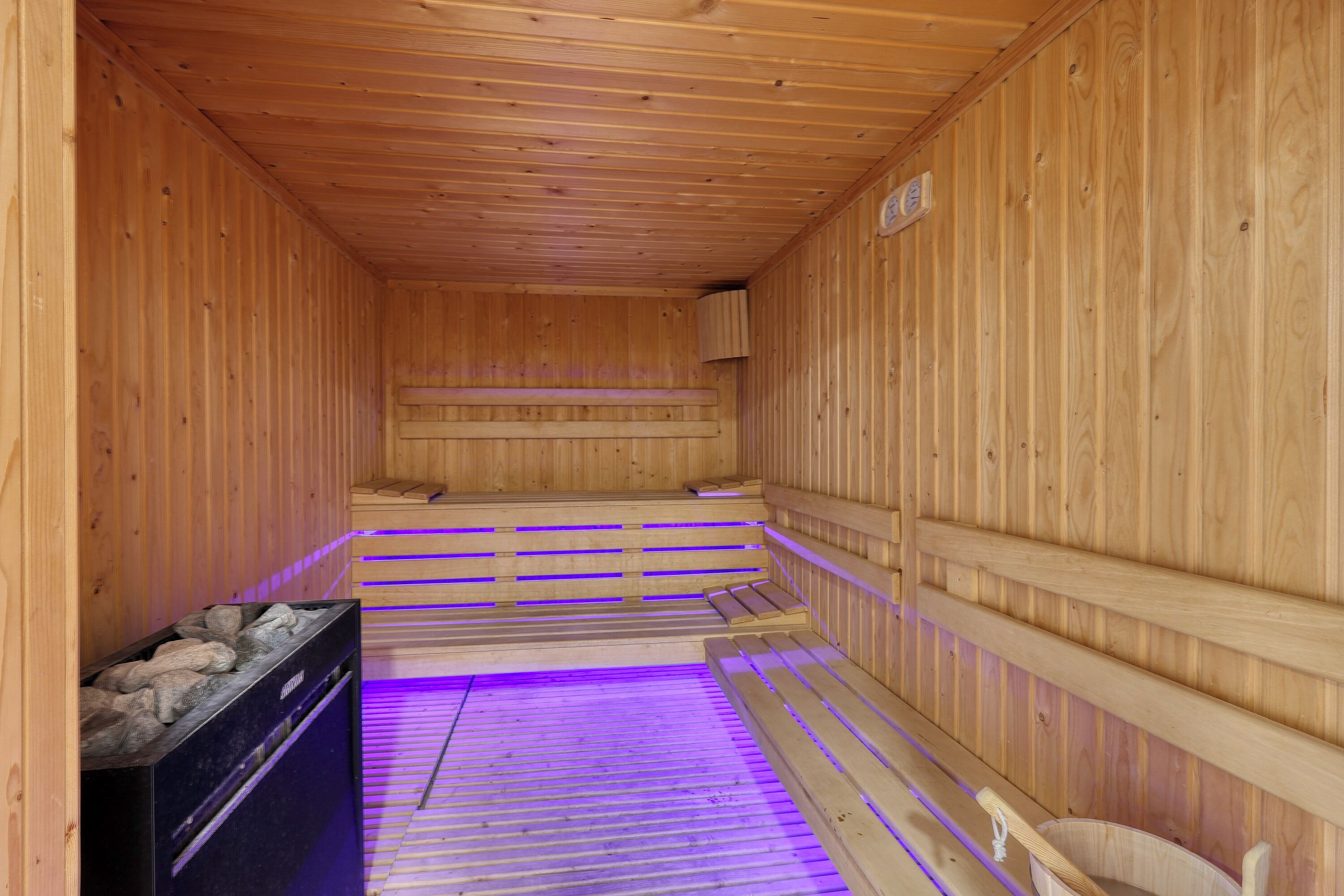 Una sauna con paredes y bancos de madera, suelo con calefacción y una pileta de piedra.