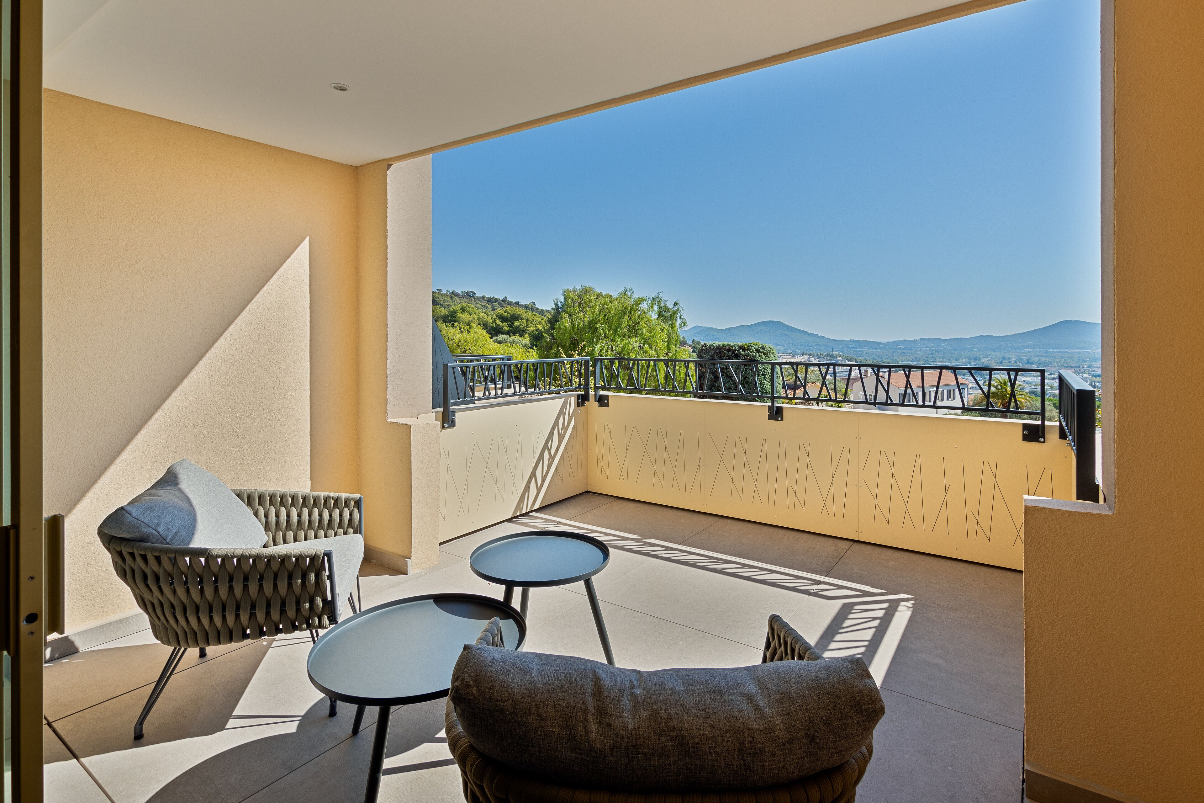 Een balkon met uitzicht op bergen, een stoel, een tafeltje en een hekwerk.