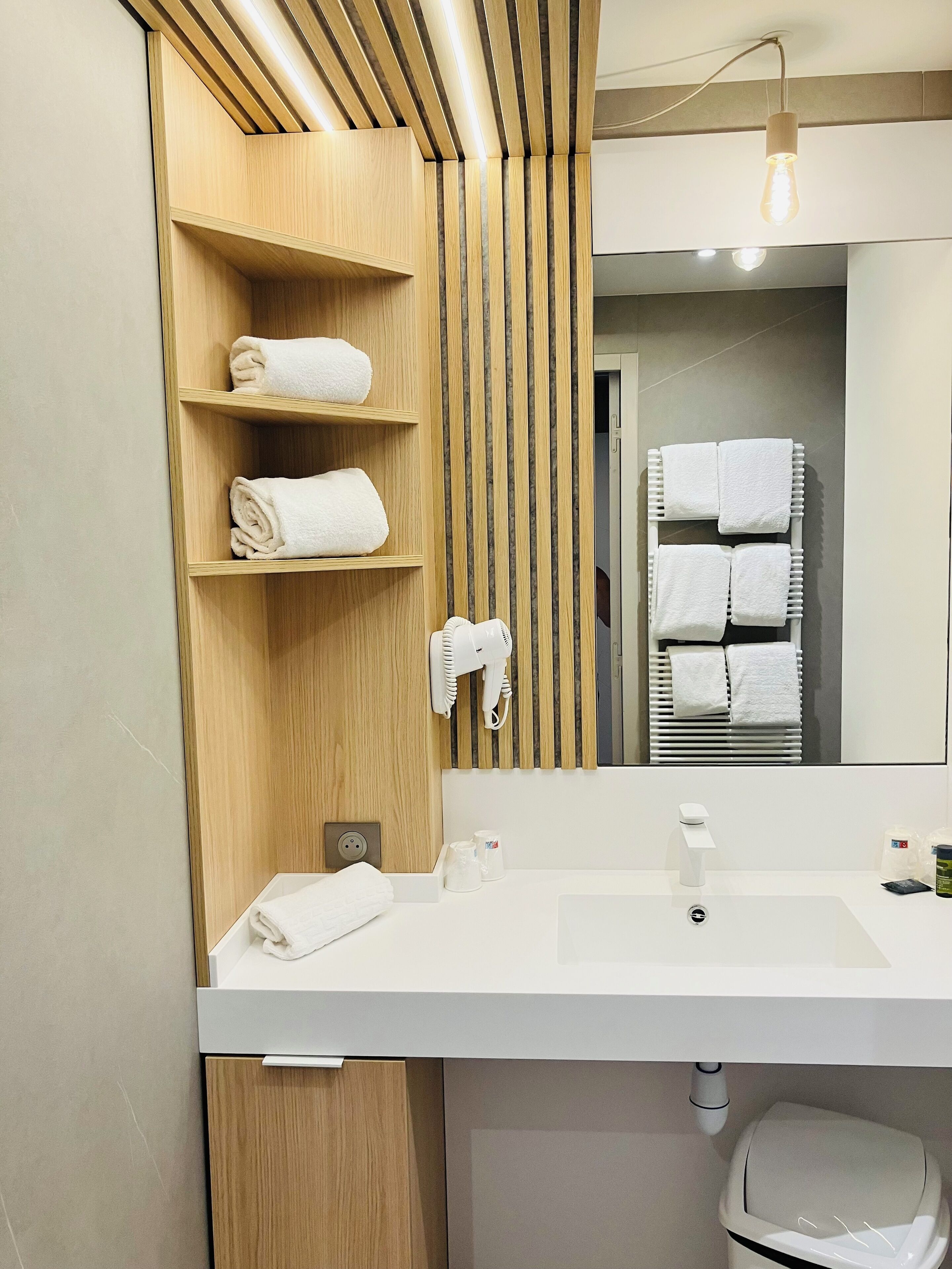Un baño moderno con tocador de madera, un espejo, un perchero para toallas y un lavabo.