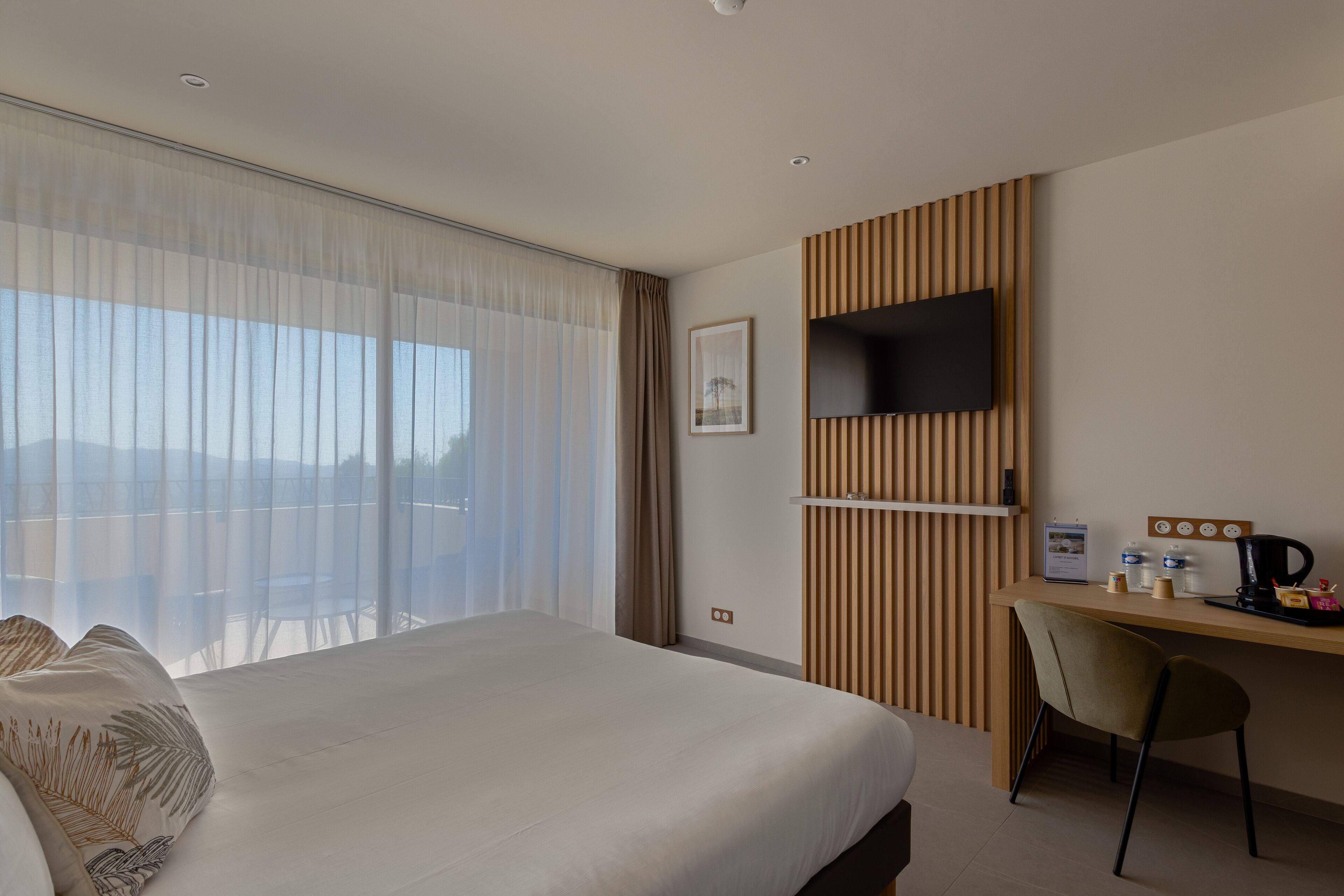 Une chambre d’hôtel dotée d’un grand lit, d’un bureau avec un téléviseur à écran plat, d’une chaise et offrant une vue sur l’extérieur.