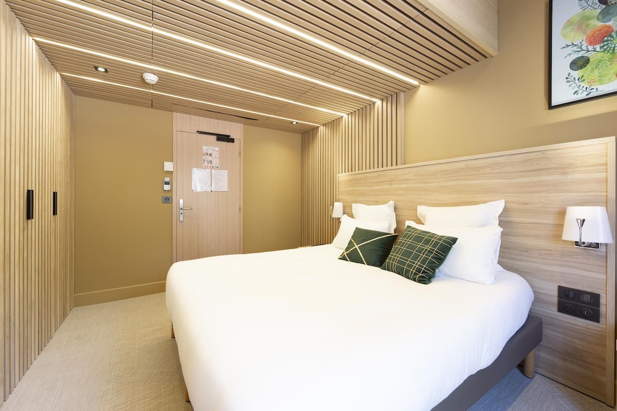 Ein Hotelzimmer mit einem großen Bett, einem Holzkopfteil und einer Decke mit linearer Beleuchtung.