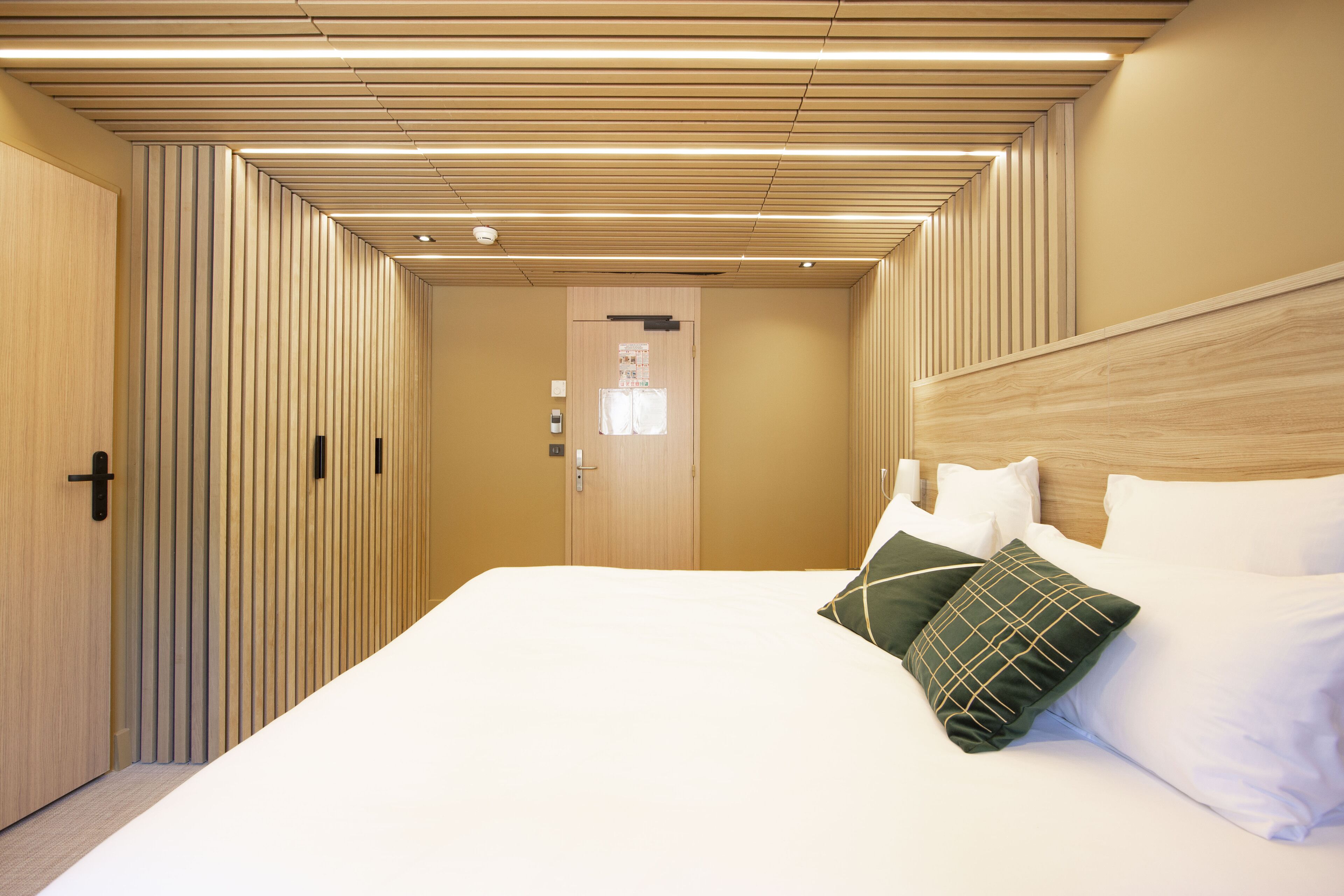 Una habitación de hotel con techo de listones de madera, una cama grande con ropa blanca y cabecera de madera.
