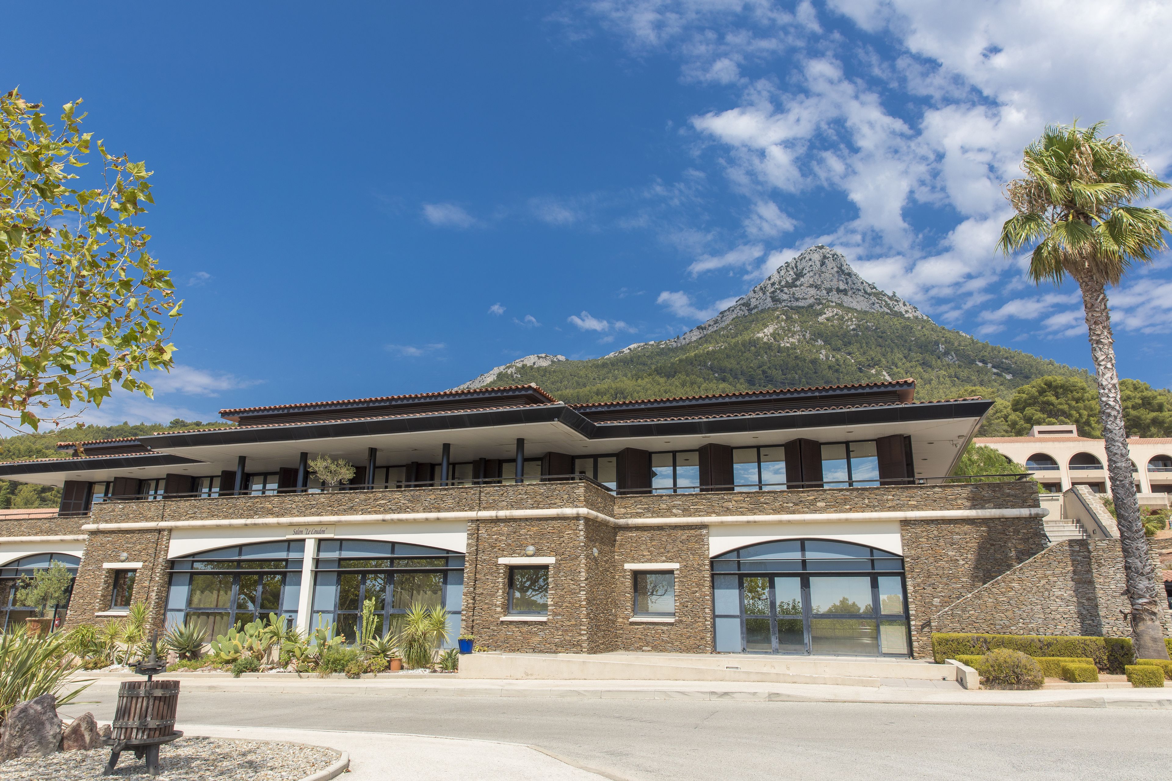 A modern hotel with a stone facade, large windows, and a mountain backdrop.