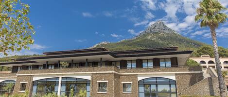 A modern hotel with a stone facade, large windows, and a mountain backdrop.