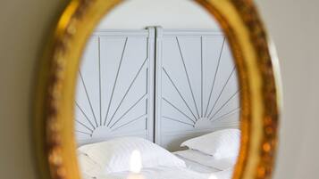 Un espejo de marco decorado refleja una cama con ropa de cama blanca y dos velas encendidas.