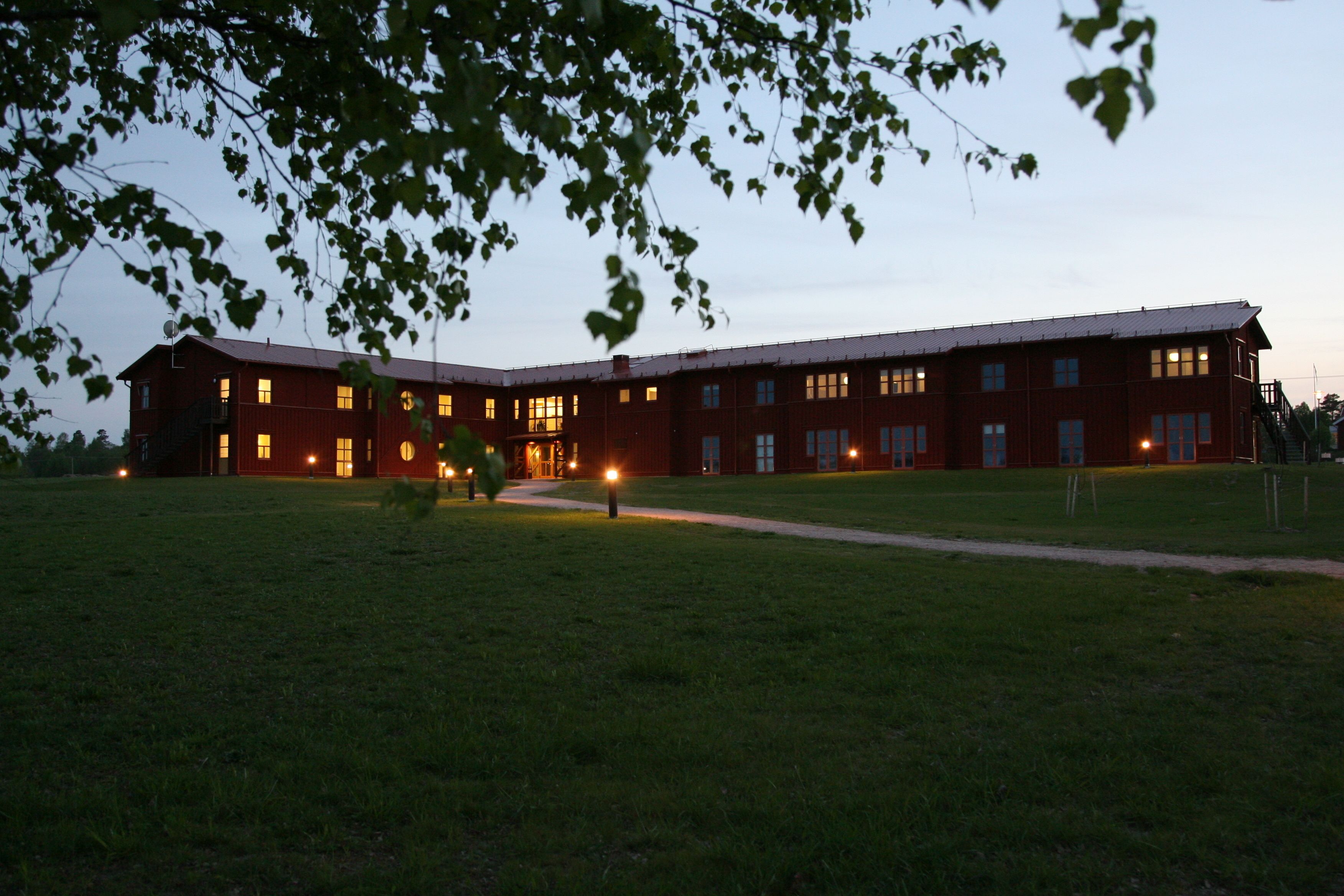 A large, multi-story building with a red exterior and multiple windows, surrounded by a grassy area.