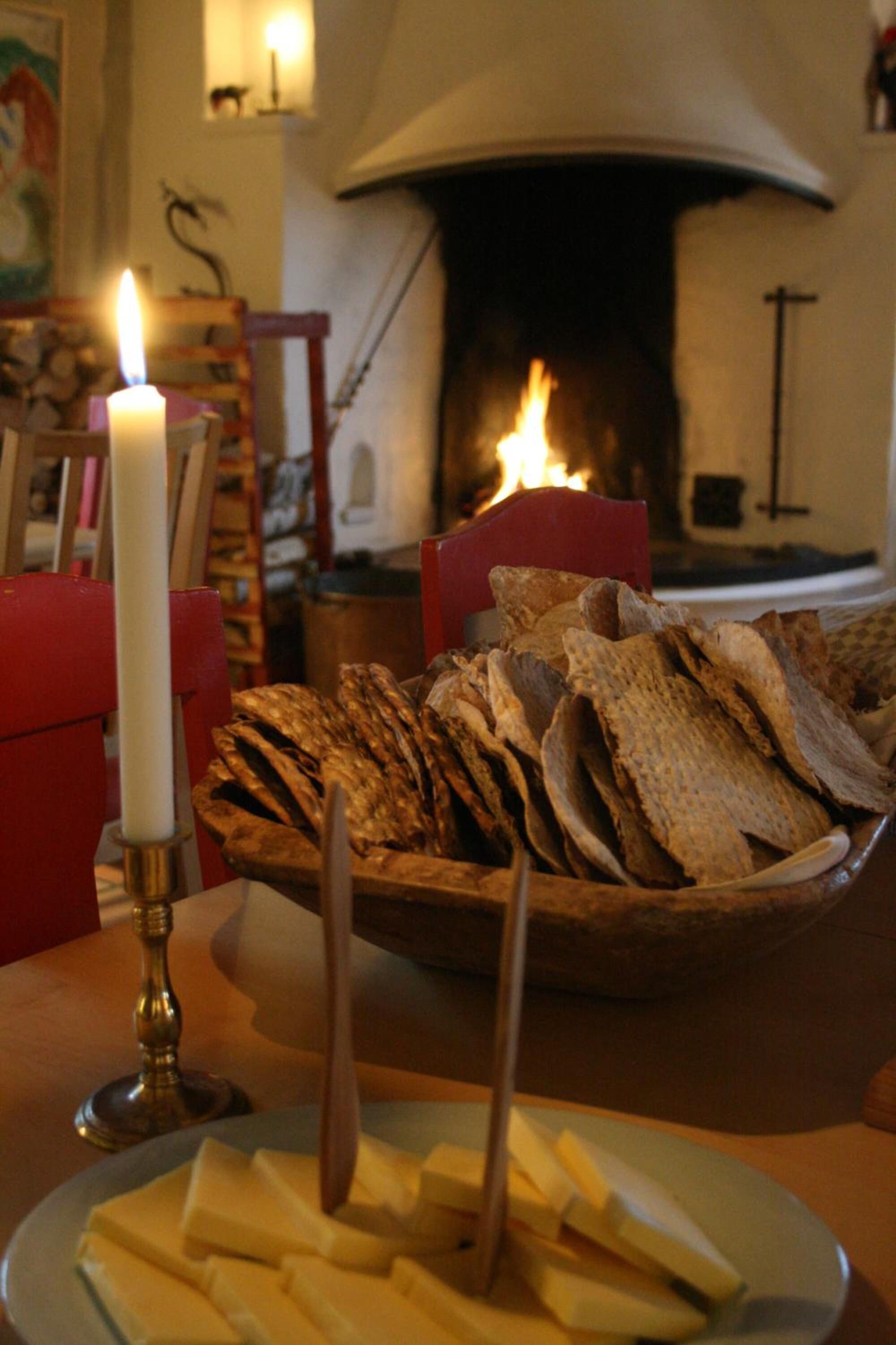 A table with a plate of cheese and crackers, a lit candle, and a fireplace in the background.