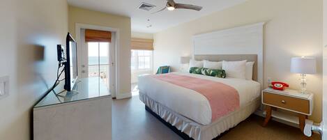 A hotel room with a bed, a desk with a computer, a telephone, and a ceiling fan.