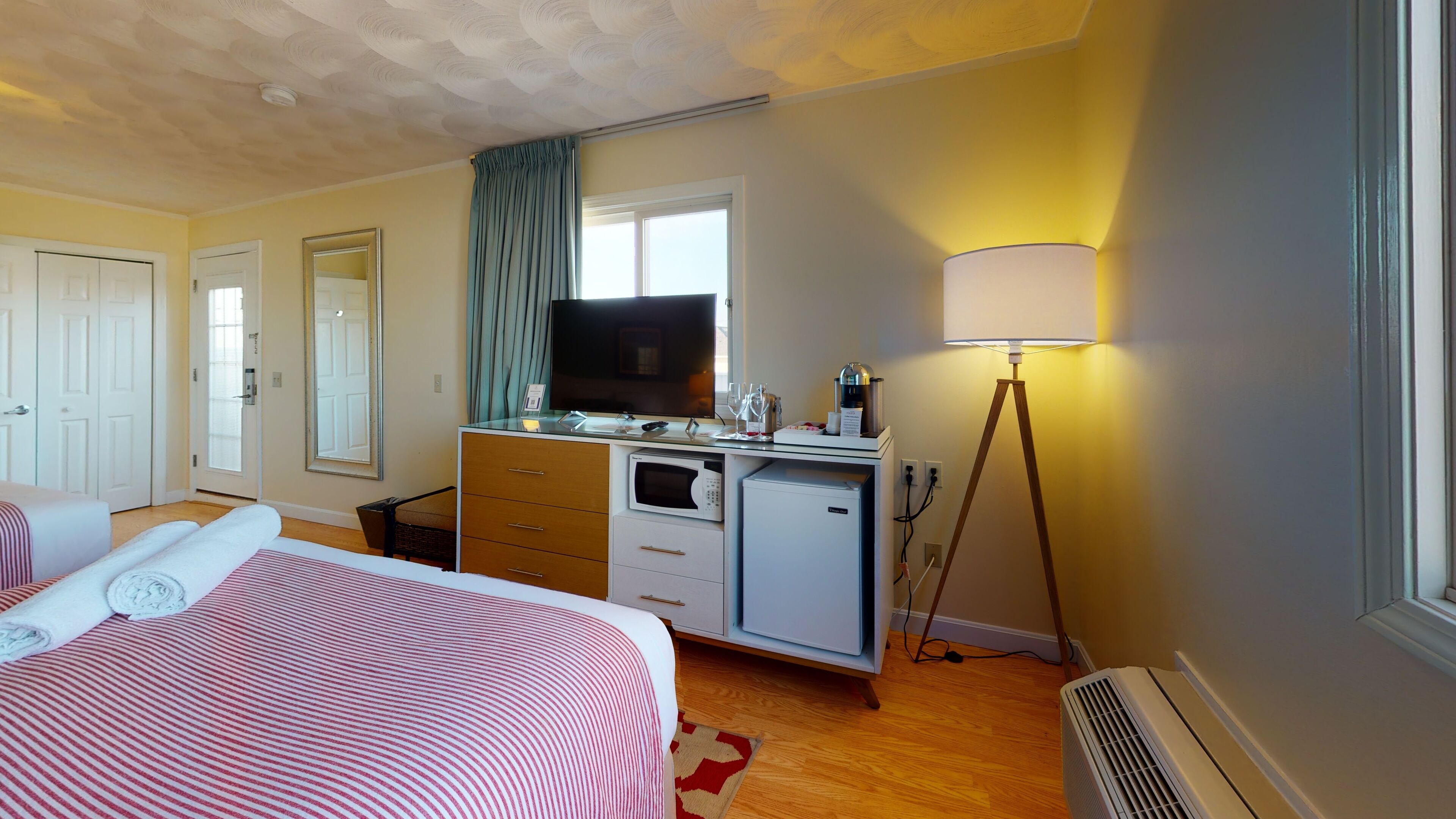 A hotel room with a bed, a desk with a TV, a microwave, a lamp, and a heater.