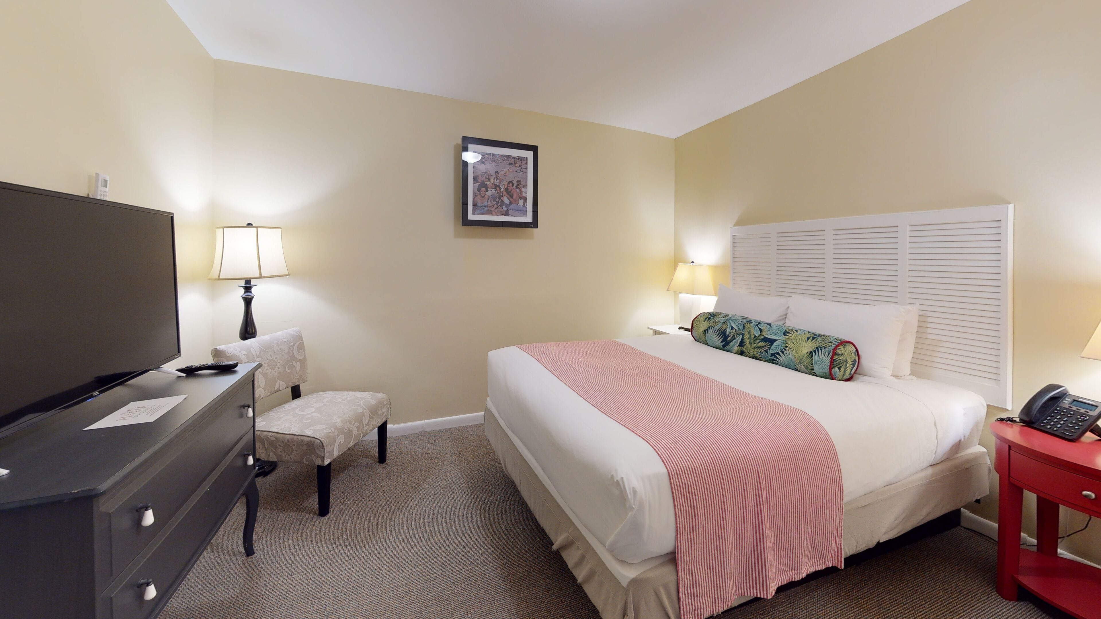 Une chambre d’hôtel comprenant un lit, un bureau avec une lampe, une chaise, un téléviseur et un téléphone.